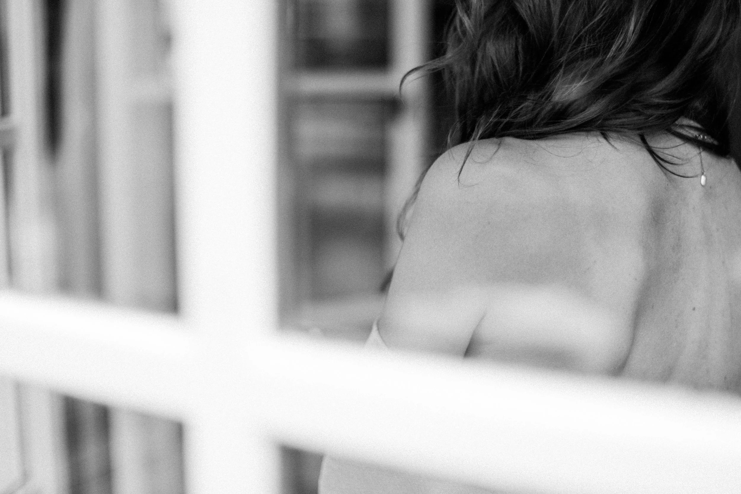 Schwarz-Weiß-Fotografie eines Frauenrückens mit lockigem Haar, die an einer Wand steht.
