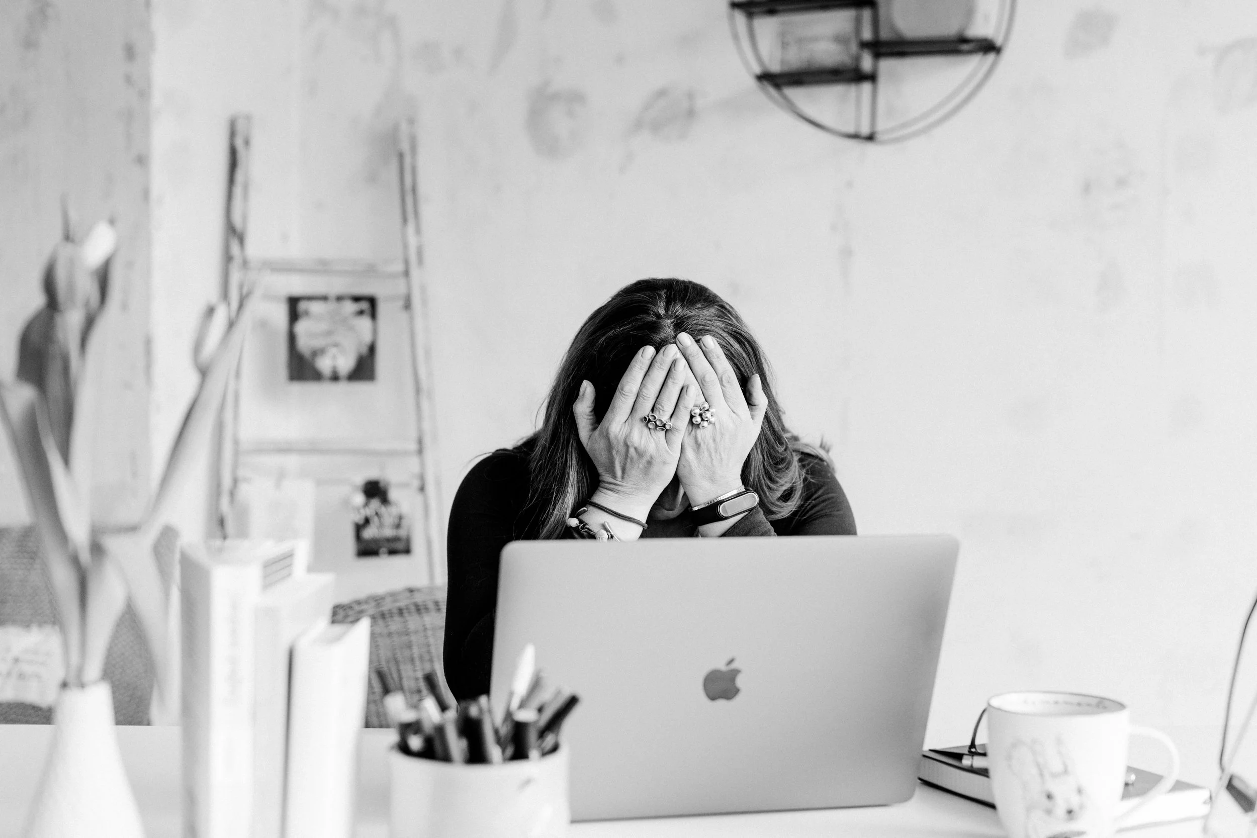 Frau sitzt am Schreibtisch, hält sich mit den Händen den Kopf und wirkt gestresst vor einem Laptop.