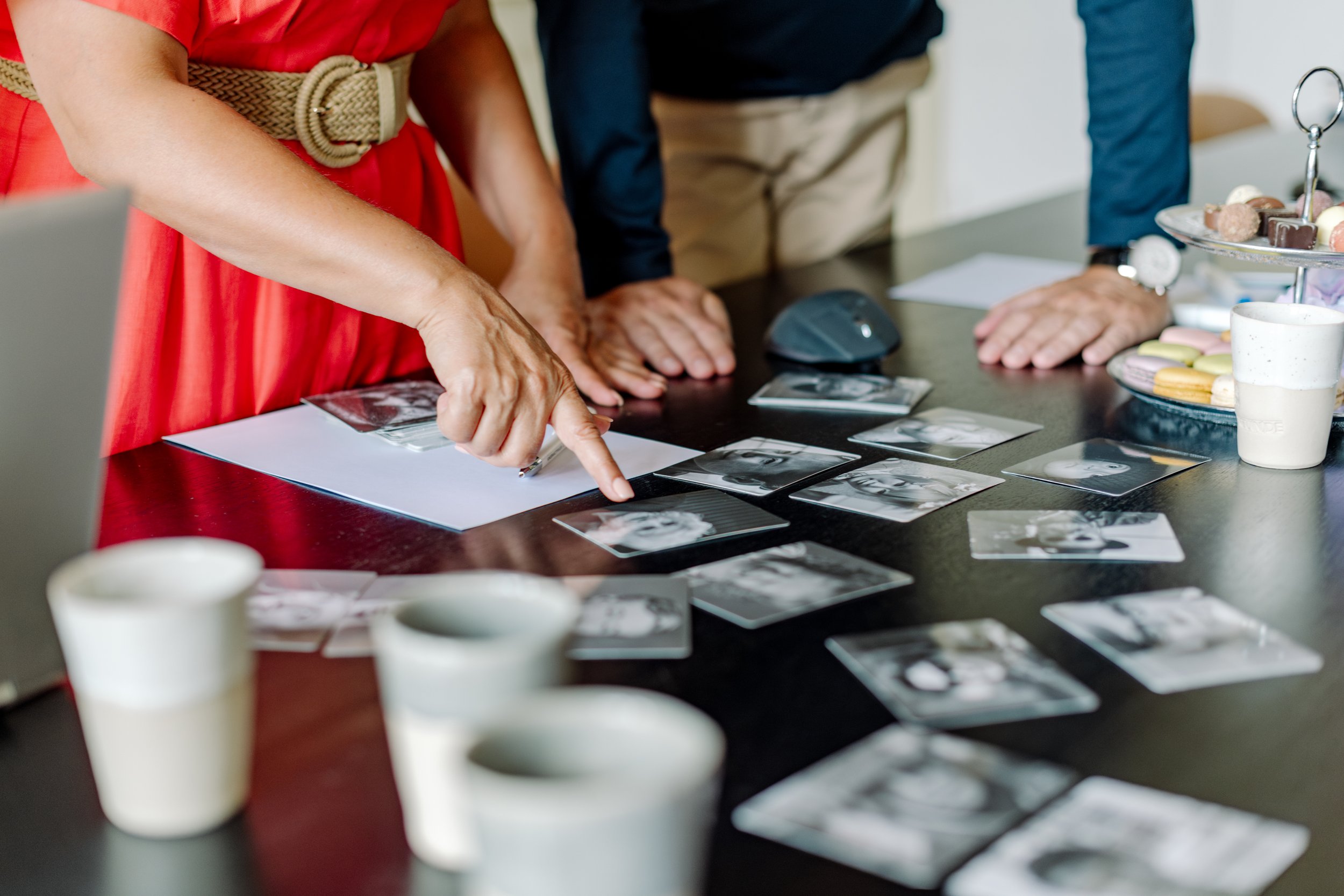 Menschen besprechen Gefühle-Karten mit schwarz-weiß Fotografien auf einem Tisch, umgeben von Süßigkeiten und Kaffeetassen.