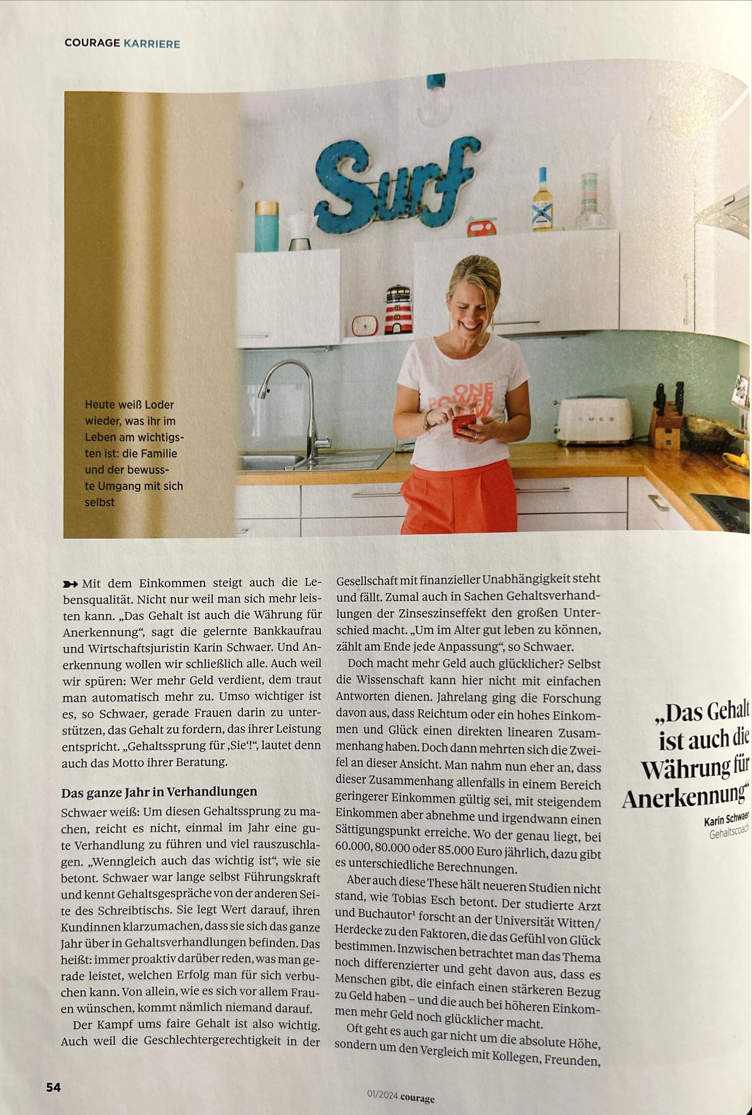 Eine Frau steht in einer hellen modernen Küche, trägt ein weißes T-Shirt mit rotem Text und rote Shorts, lächelt und schaut auf ihr Smartphone. Im Hintergrund befinden sich weiße Küchenoberschränke, Dekorationsgegenstände, ein Wasserhahn, ein Toaster, Messer und andere Küchengeräte, sowie ein großes Wandschild mit dem Wort „Surf“ in blauer Schrift.