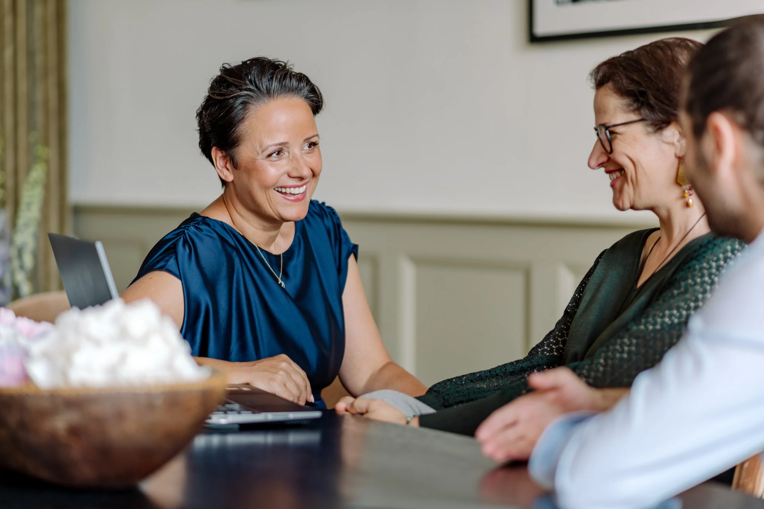 Zwei Frauen und ein Mann sitzen an einem Tisch, die Frauen lachen und führen ein Gespräch.