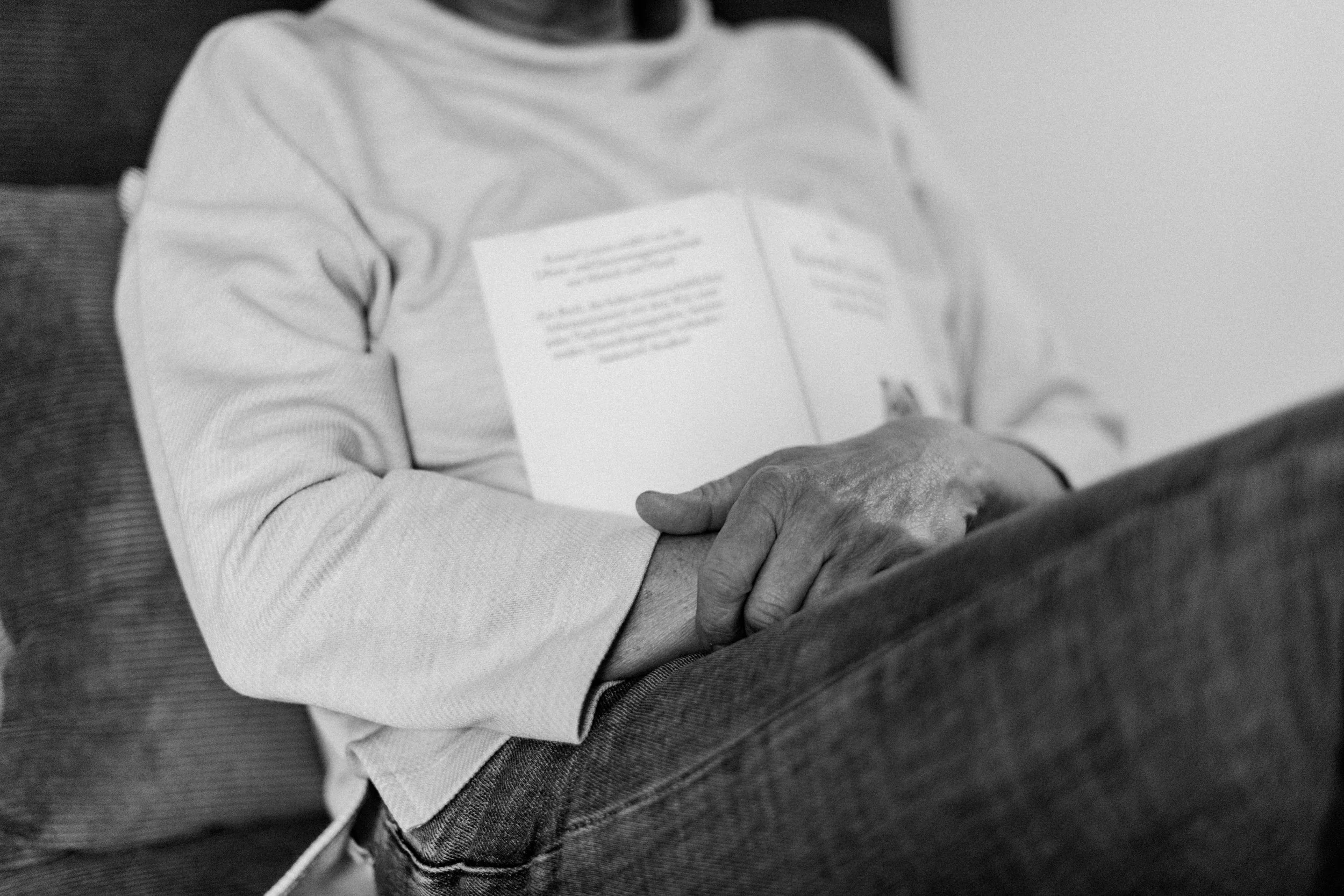 Oberkörper einer sitzenden Frau, die ein Buch auf die Brust gelegt und die Arme darüber verschränkt hat. Ein Bild in schwarz/weiß