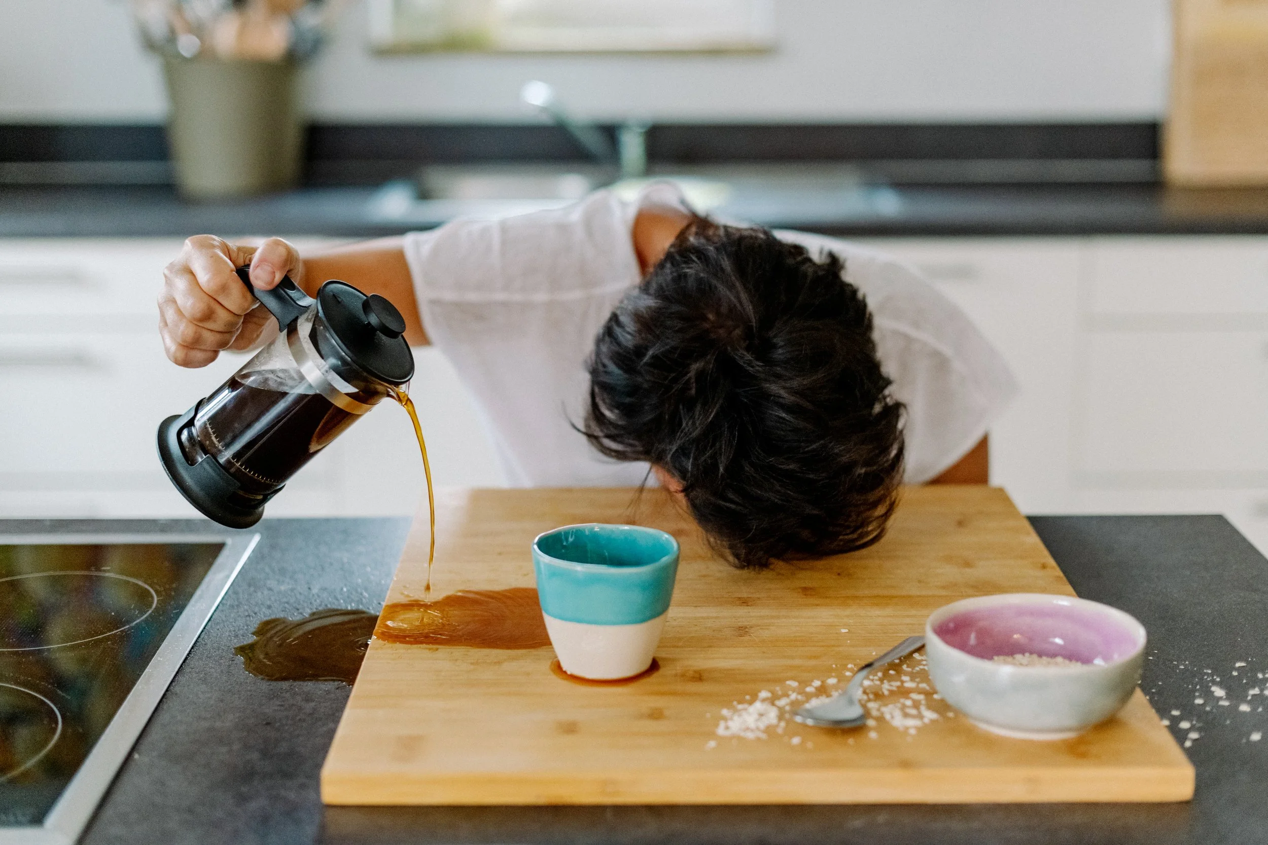 Eine Person gießt Kaffee in eine Tasse auf einer Küchenarbeitsplatte, umgeben von leeren Tassen und Küchenutensilien.