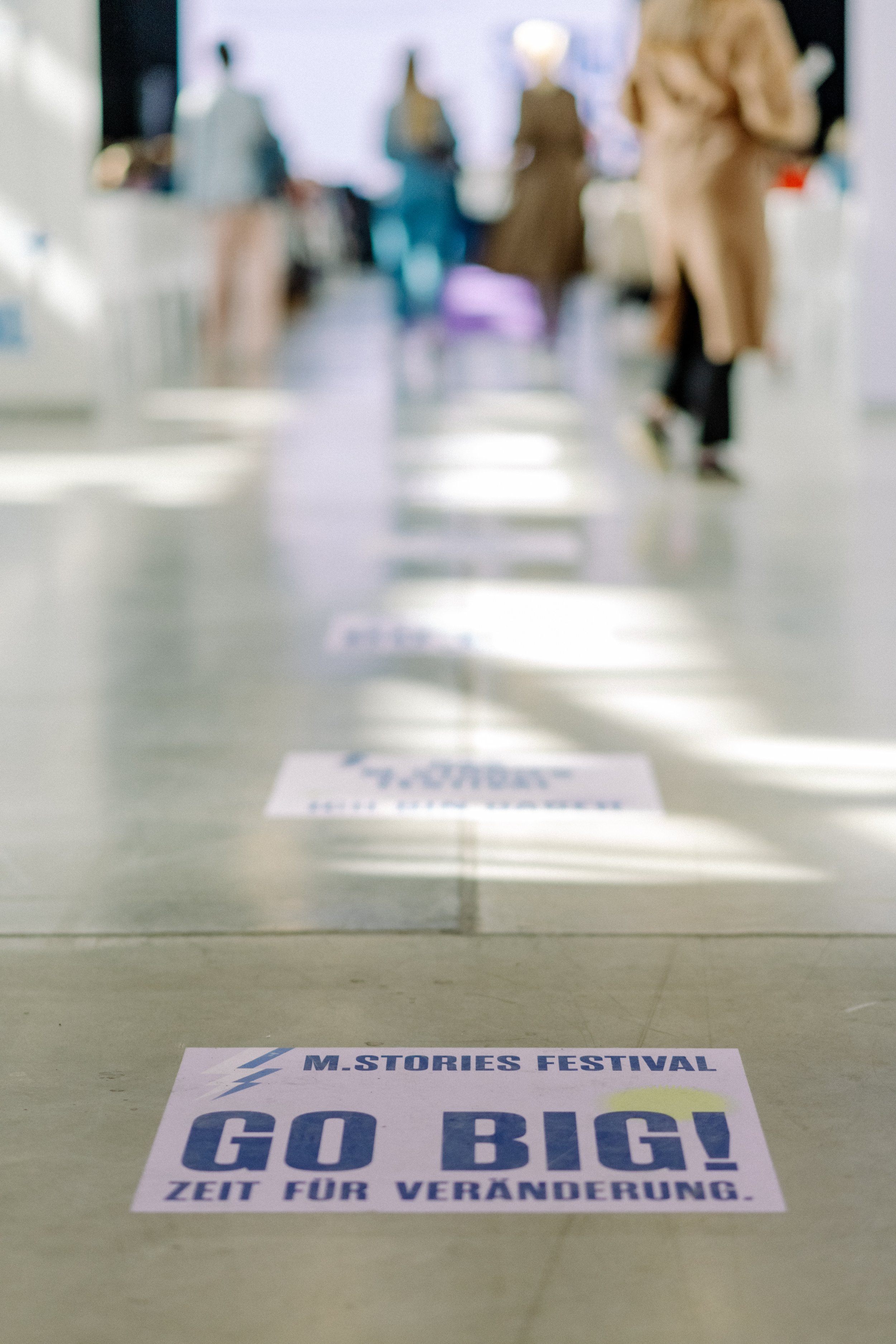 Boden mit Aufklebern, die zur Teilnahme am M-Stories Festival aufrufen, mit Schriftzug 'GO BIG! Zeit für Veränderung'