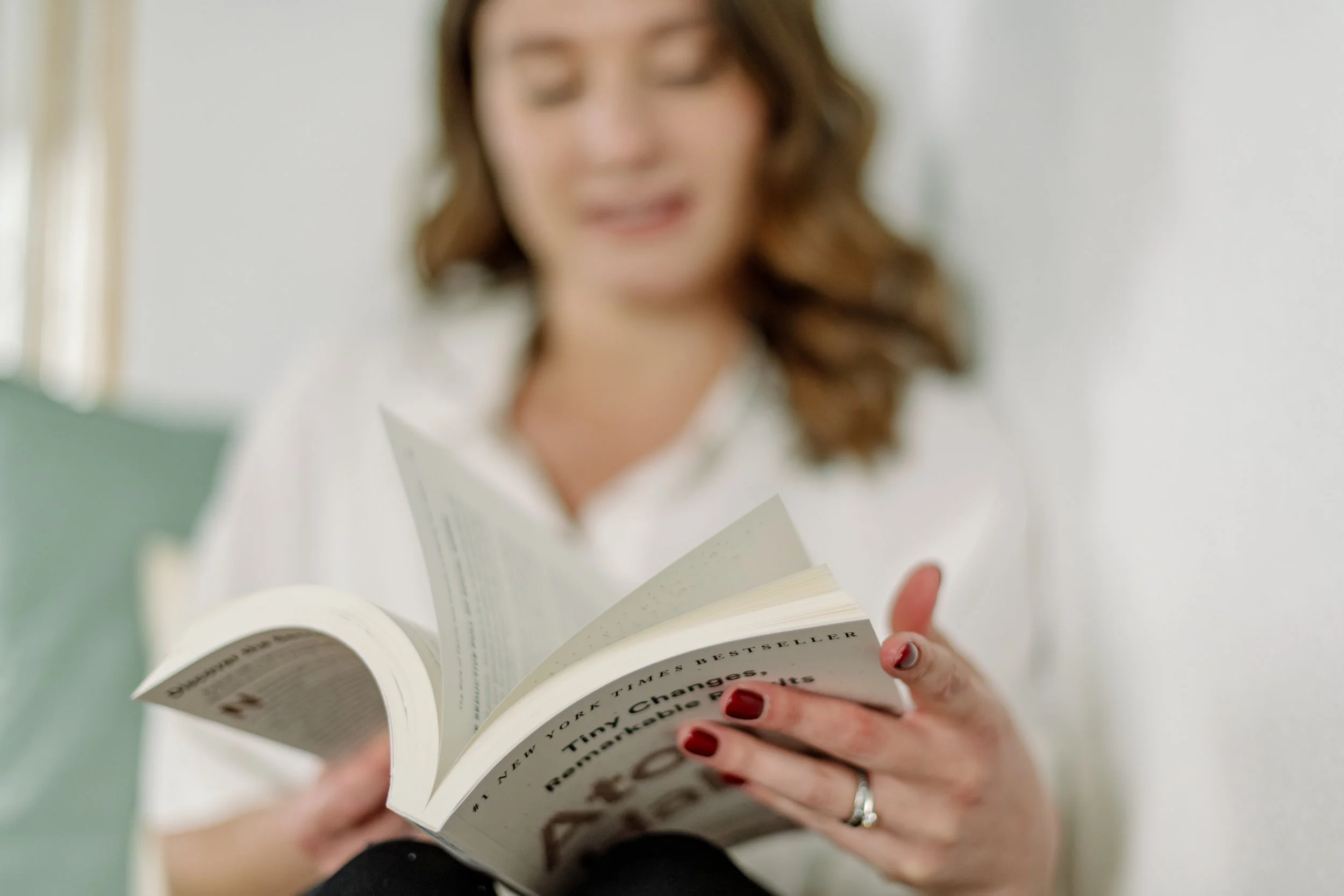 Nahaufnahme einer Frau mit roten Nägeln, die ein Buch liest, die Sicht und ihr Gesicht sind unscharf.