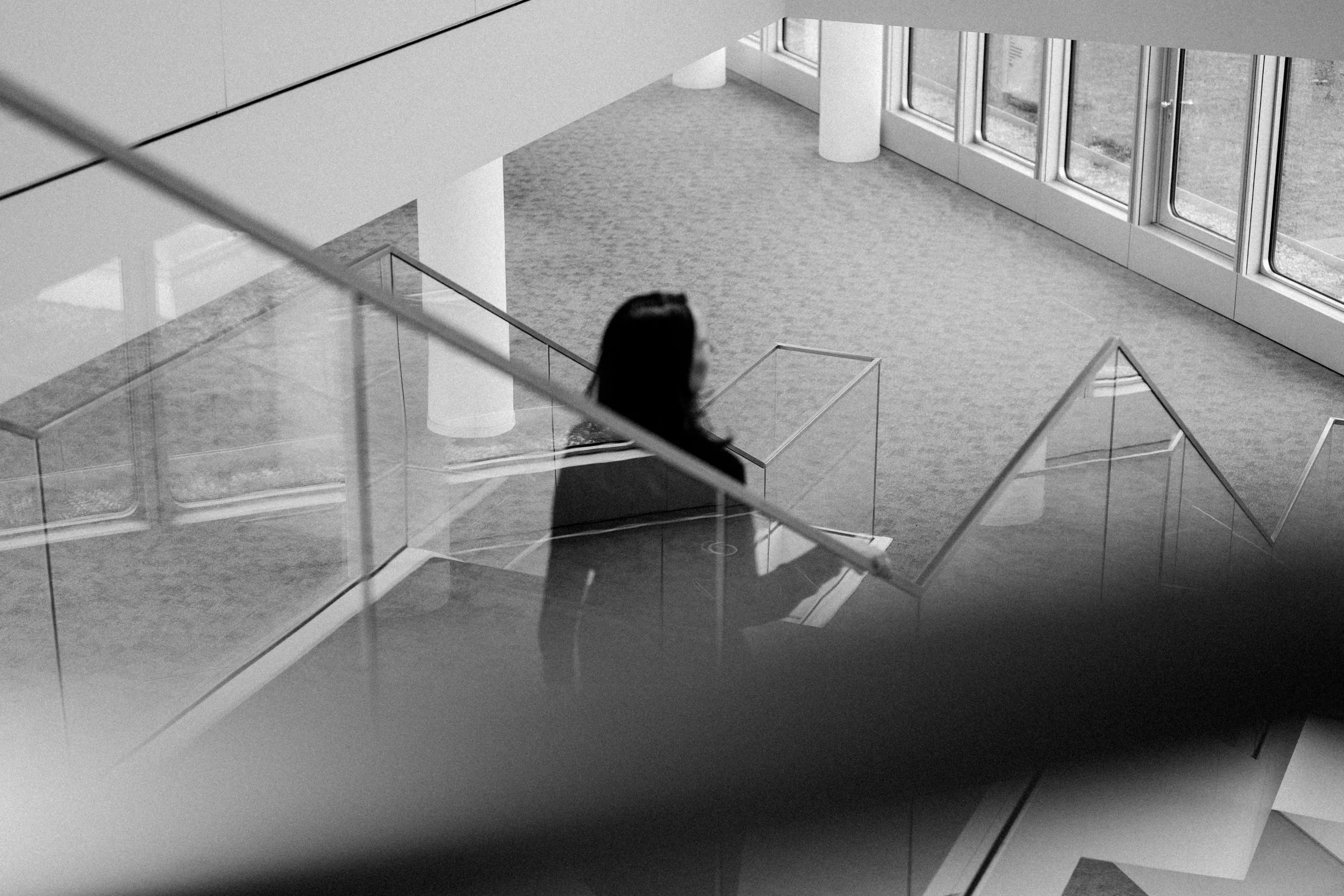 Ein Blick auf eine moderne, helle Lobby mit großen Fenstern, Glasgeländern und einer Person, die nach vorne schaut.