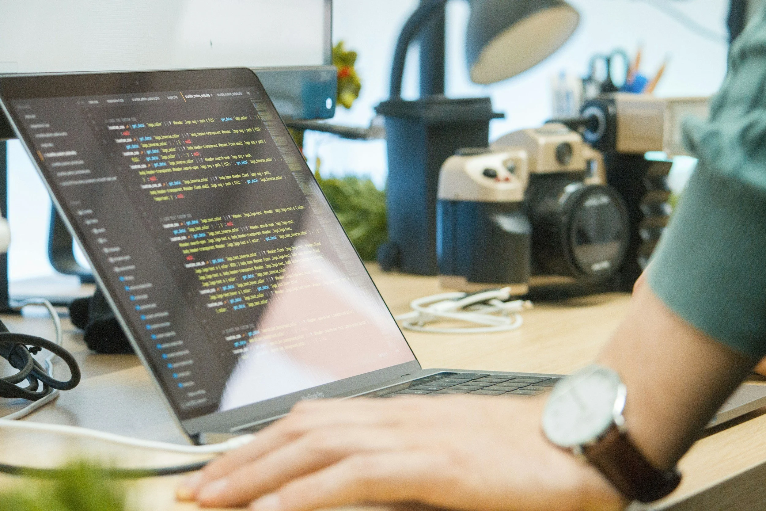 Person working on a MacBook with programming code displayed on the screen in an office setting.