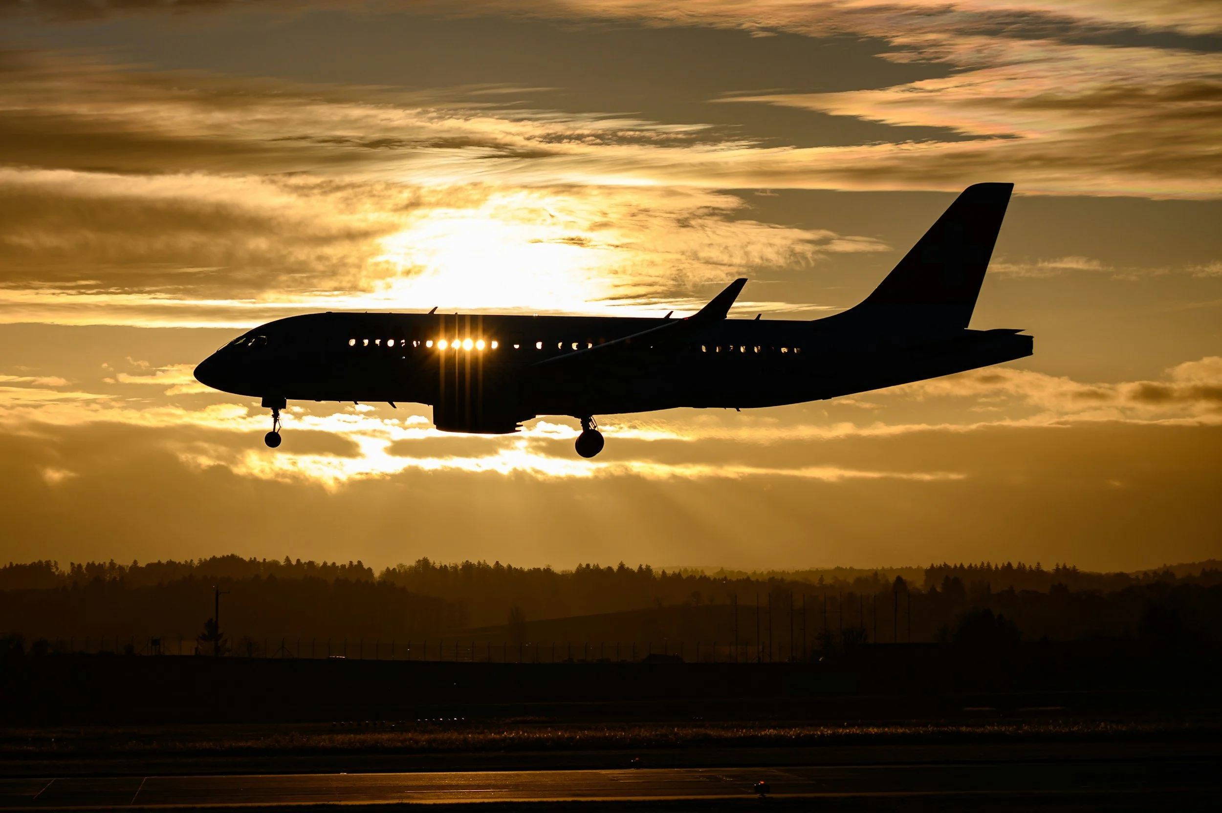 Silhouette of an airplane landing or taking off during sunset, with the sun behind the plane and a cloudy sky.