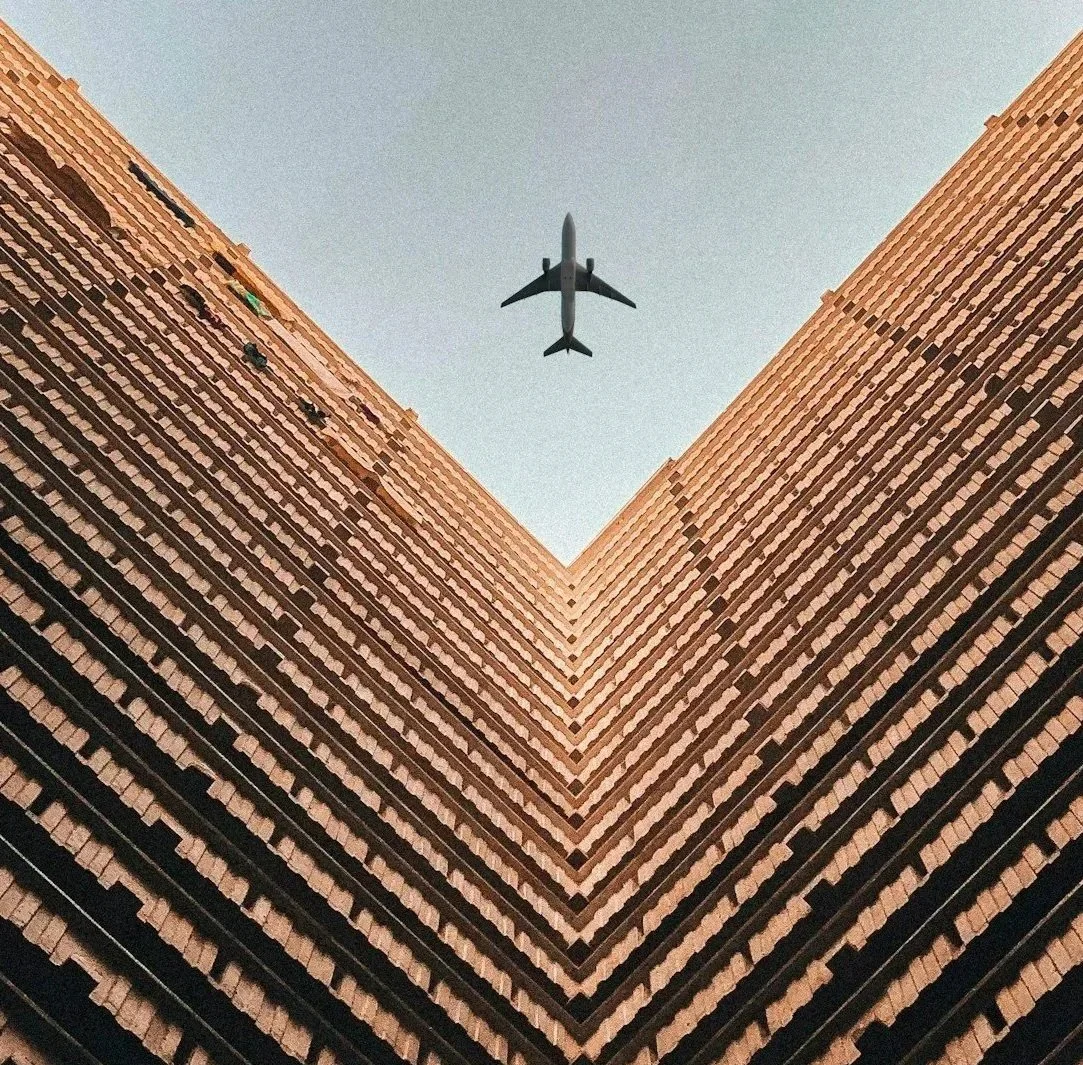 Looking up between two tall brick buildings with an airplane flying overhead in the sky.