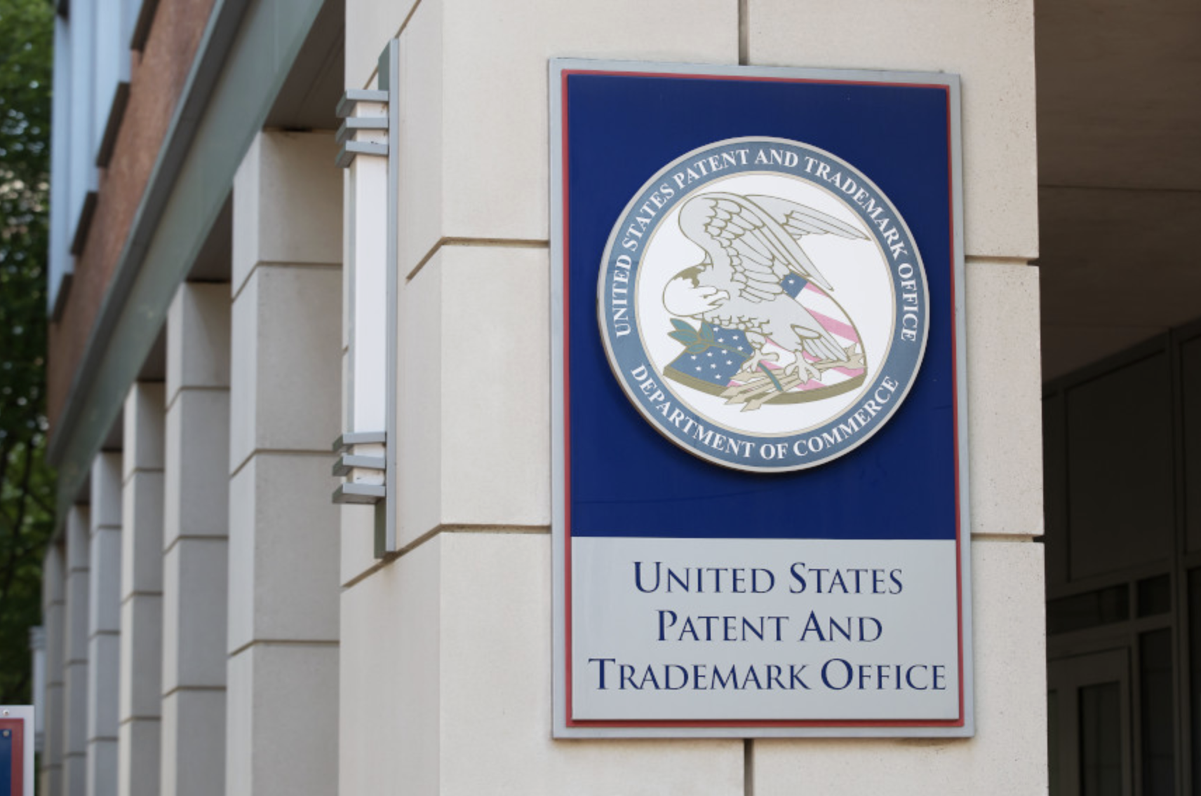 Sign for the United States Patent and Trademark Office, Department of Commerce, mounted on a beige wall outside the building.