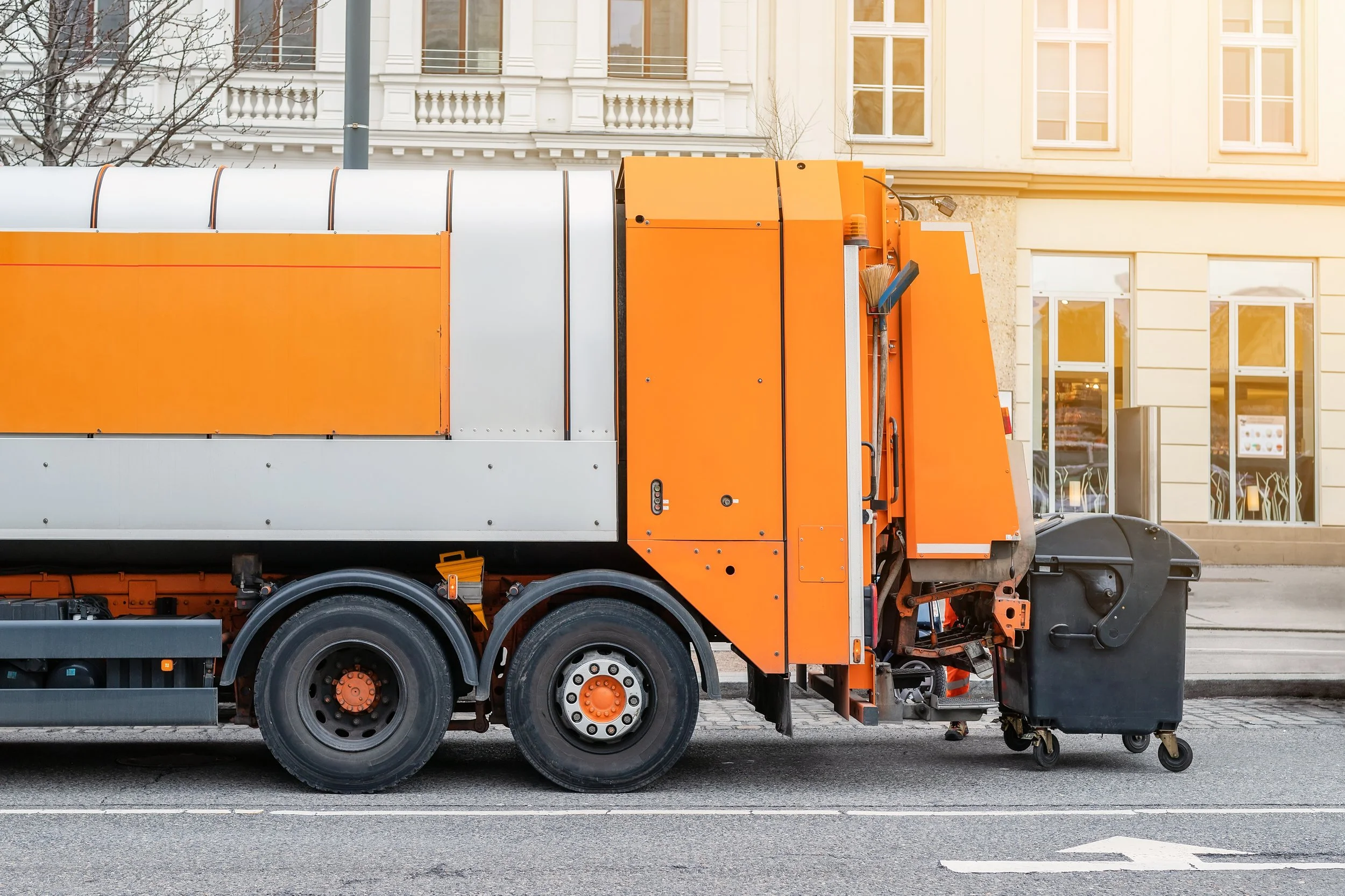 Street cleaning vehicle with orange and gray exterior, parked on city street with buildings in the background.