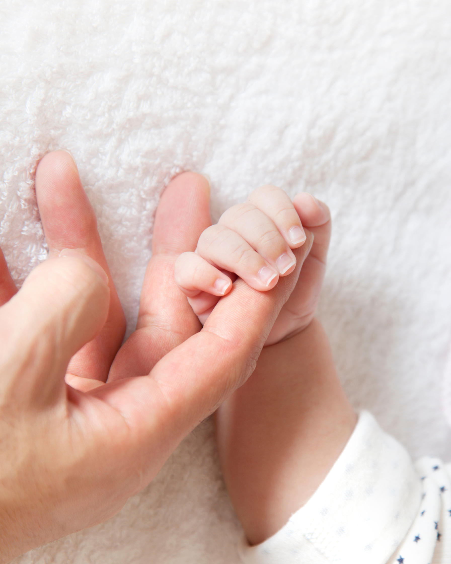 Nahaufnahme eines erwachsenen und eines kleinen Kindes, die ihre Finger miteinander verschlingen.