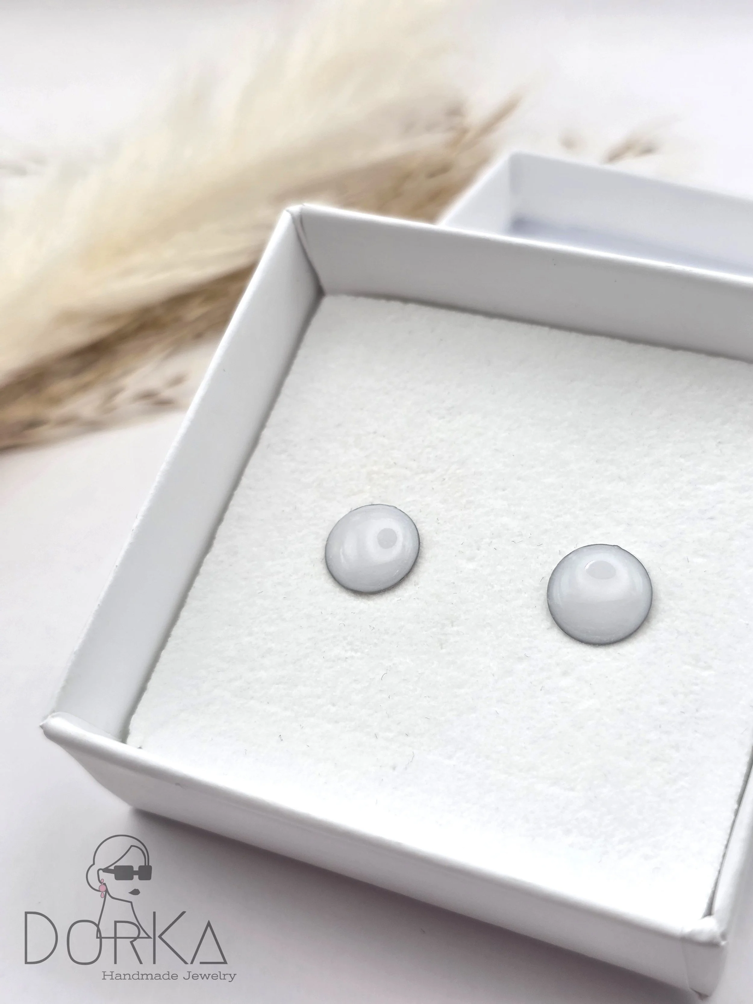 Zwei weiße perlenartige Ohrstecker in einem weißen Kasten