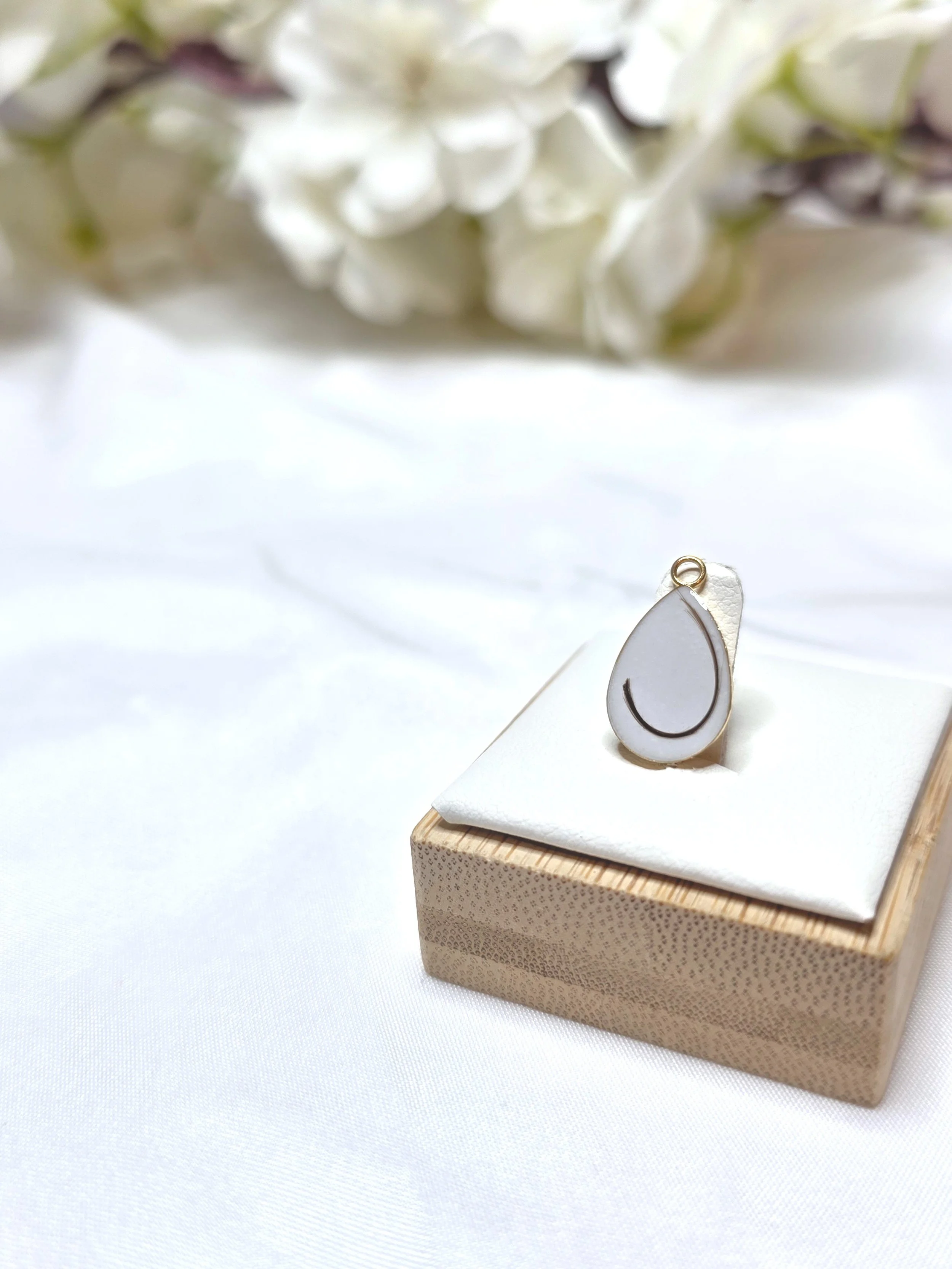 Ein paar Ohrringe auf einer kleinen weißen Polsterung, Präsentiert auf einem Holzquadrat, mit weißen Blumen im Hintergrund.