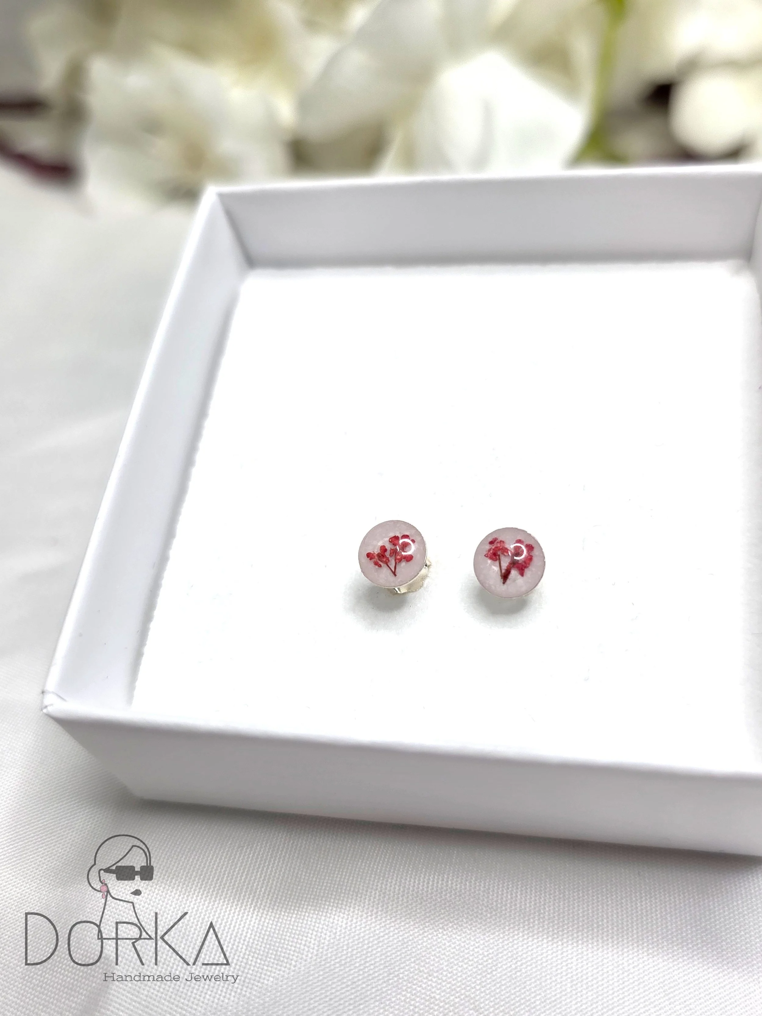 Ein weißes Schmuckkästchen mit einem Paar runder Anstecknadeln mit roten Motiven, darauf steht das Wort 'Love' in Schreibschrift.