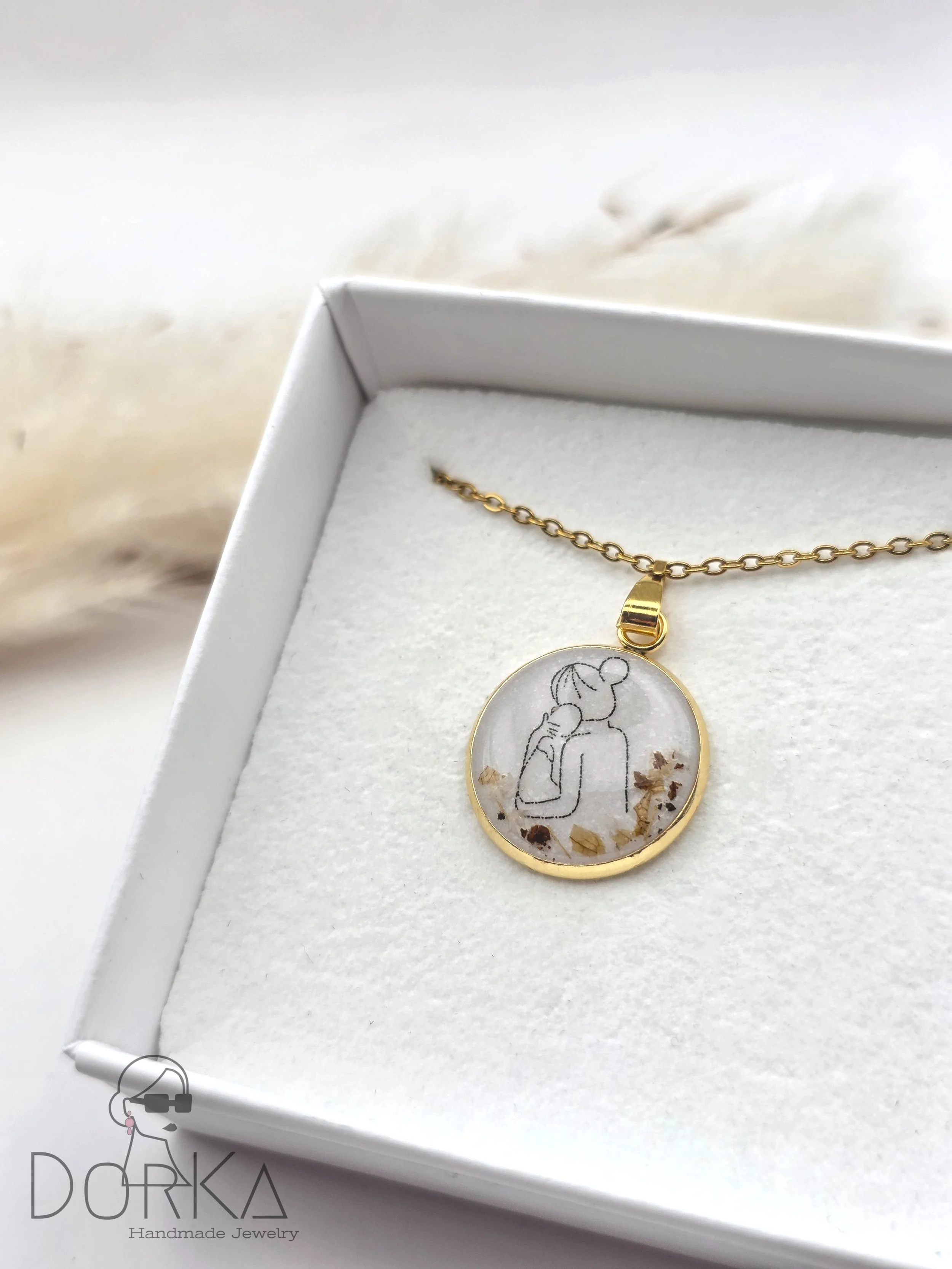 Goldene Halskette mit rundem Anhänger, der eine Silhouette einer Frau zeigt, die auf einen Arm starrt, in einem weißen Geschenkbox mit Baumwollpolster