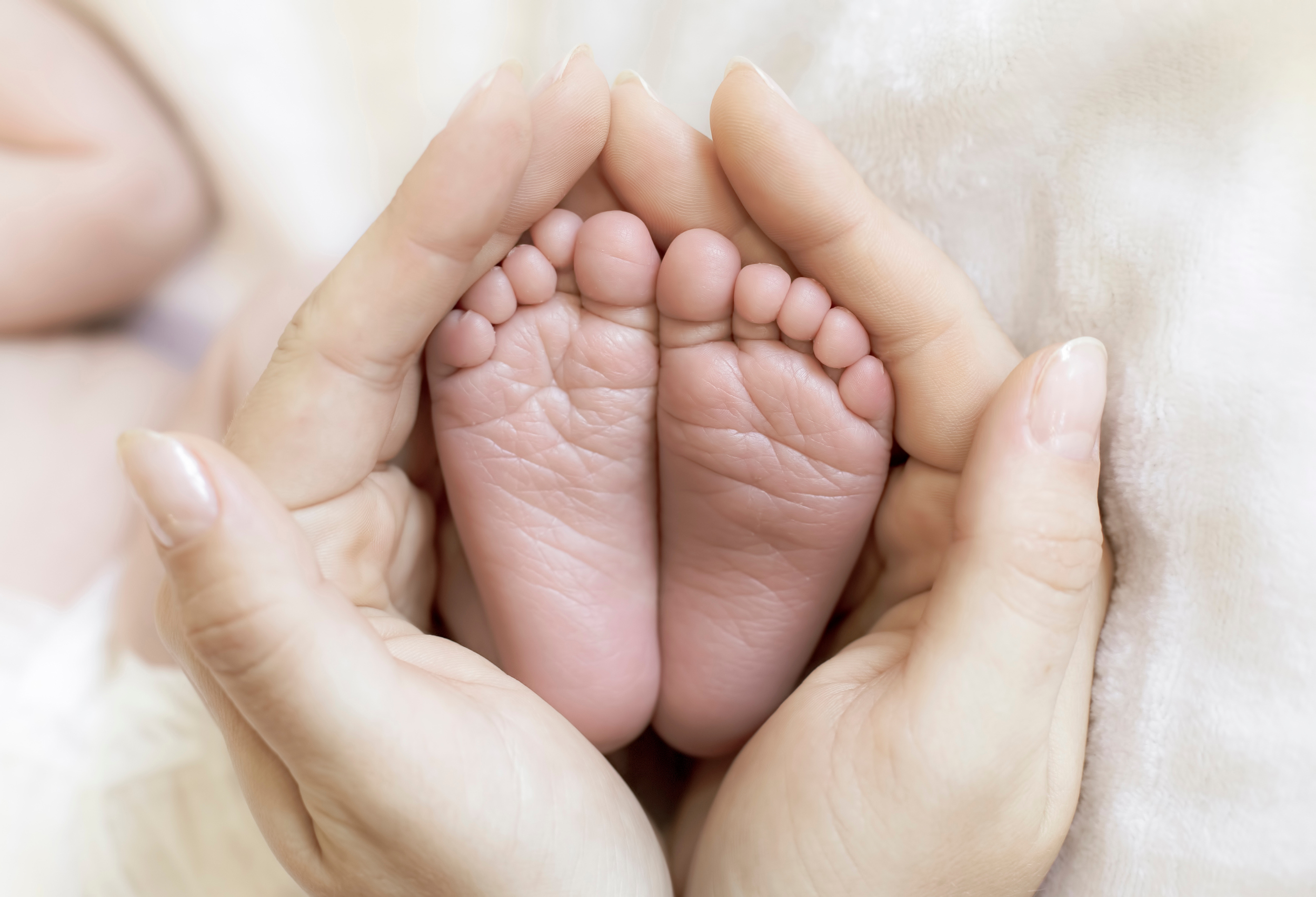 Nahaufnahme von erwachsenen Händen, die ein kleines Babyfuß in Händen halten.