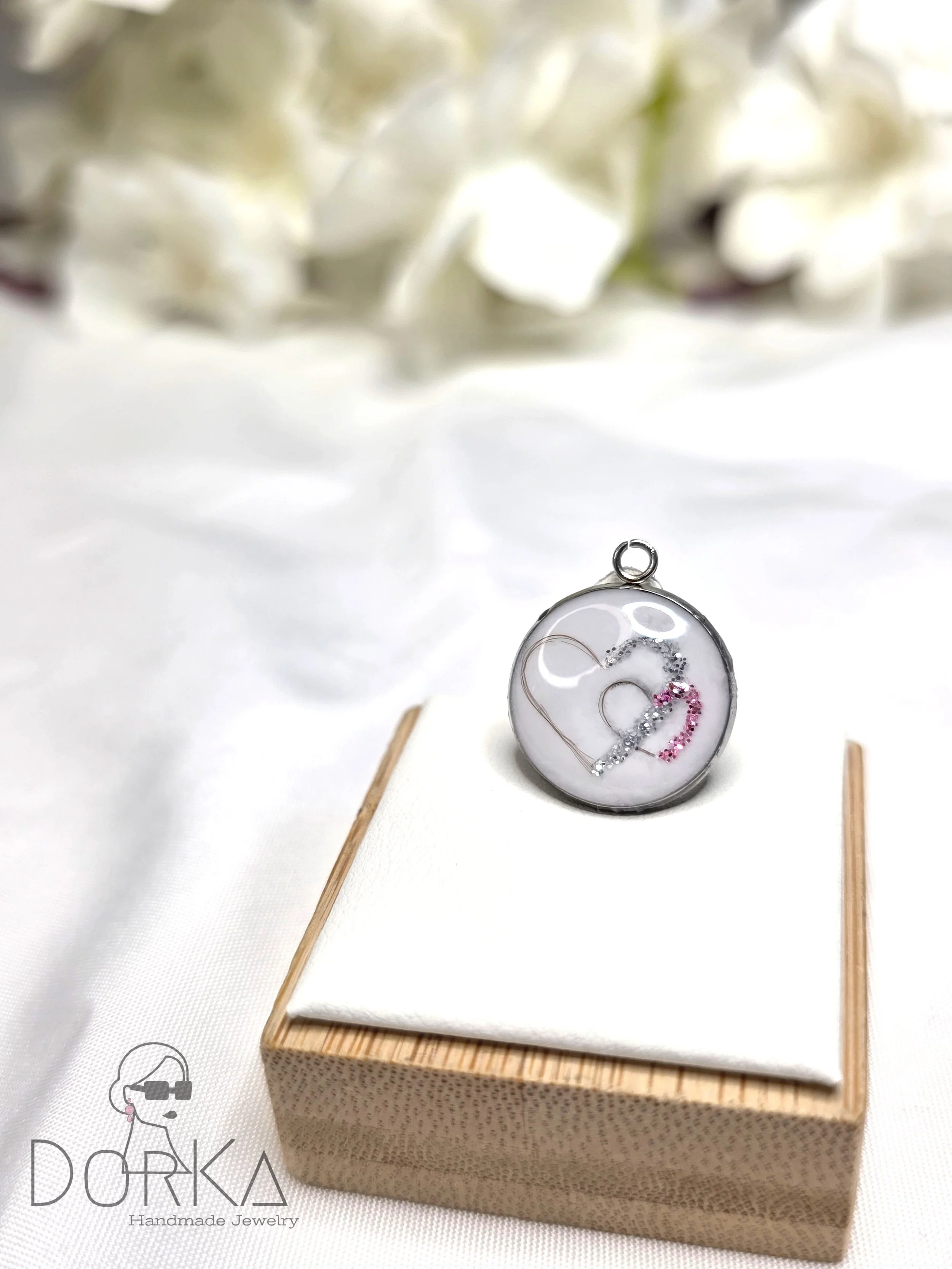 Runder Anhänger mit silbergrauem Mantel, der ein Herz mit kleinen rosa, silbernen und weißen Steinen zeigt.