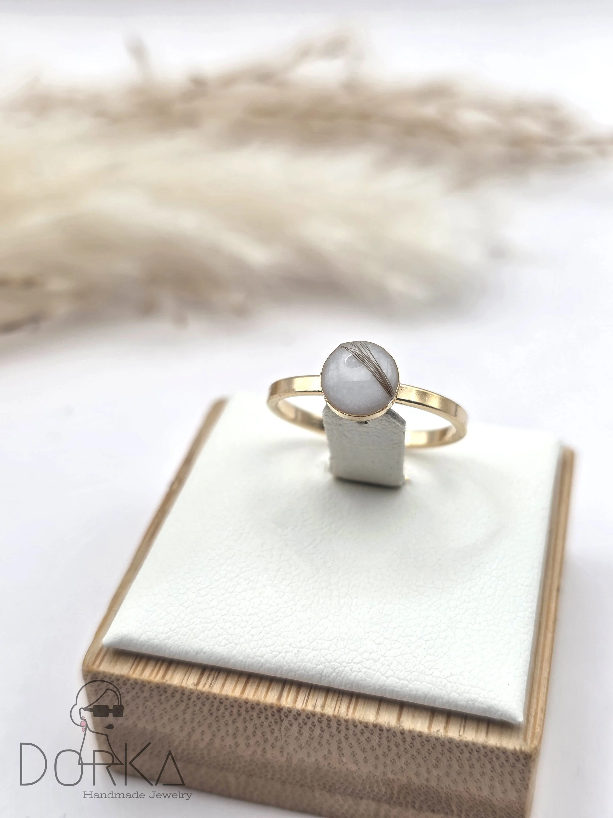 Goldring mit weißem Stein und Filigran-Detail, auf weißen Samtpolster in einem kleinen Schmuckkästchen.