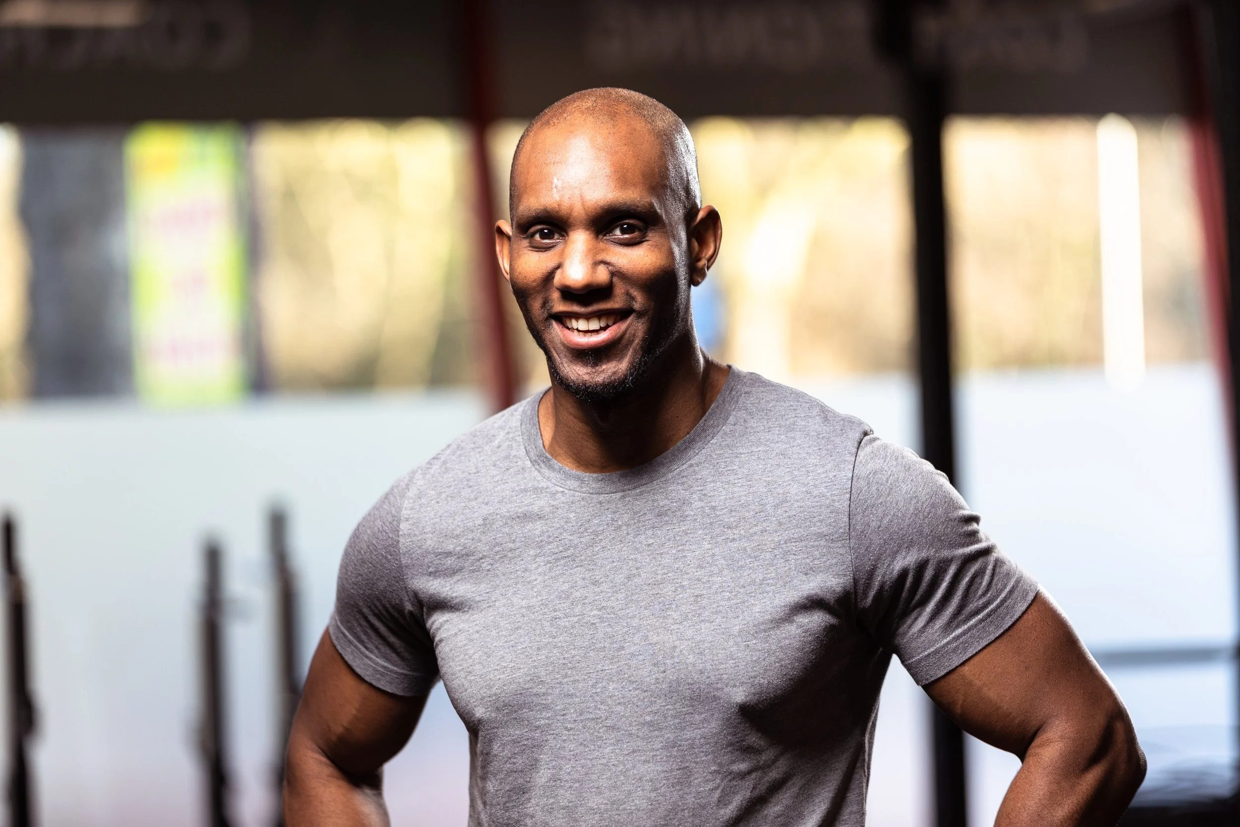 A smiling man in a gray t-shirt standing in a gym.