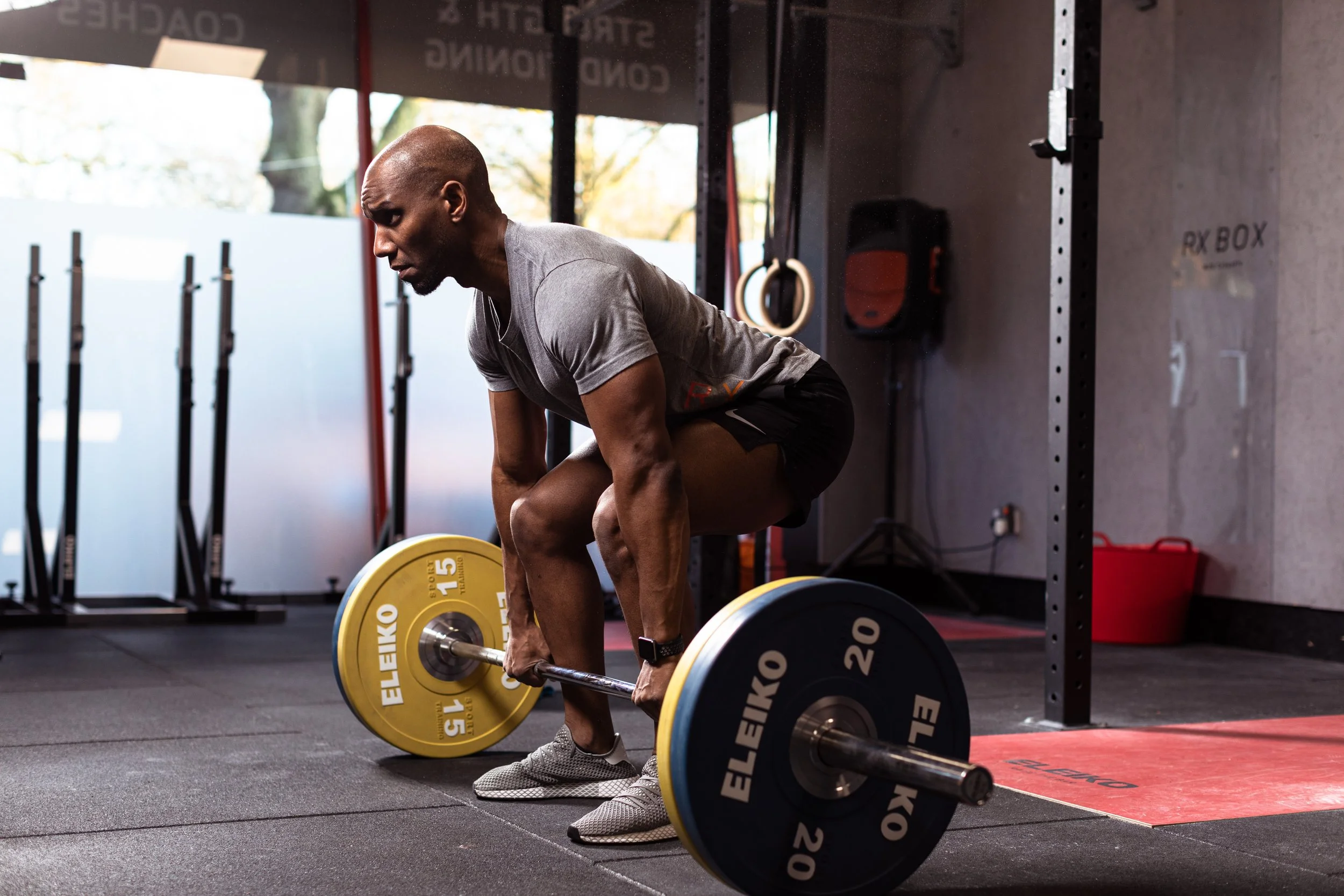 A man lifting a barbell with yellow and black weights in a gym, preparing for a deadlift exercise.