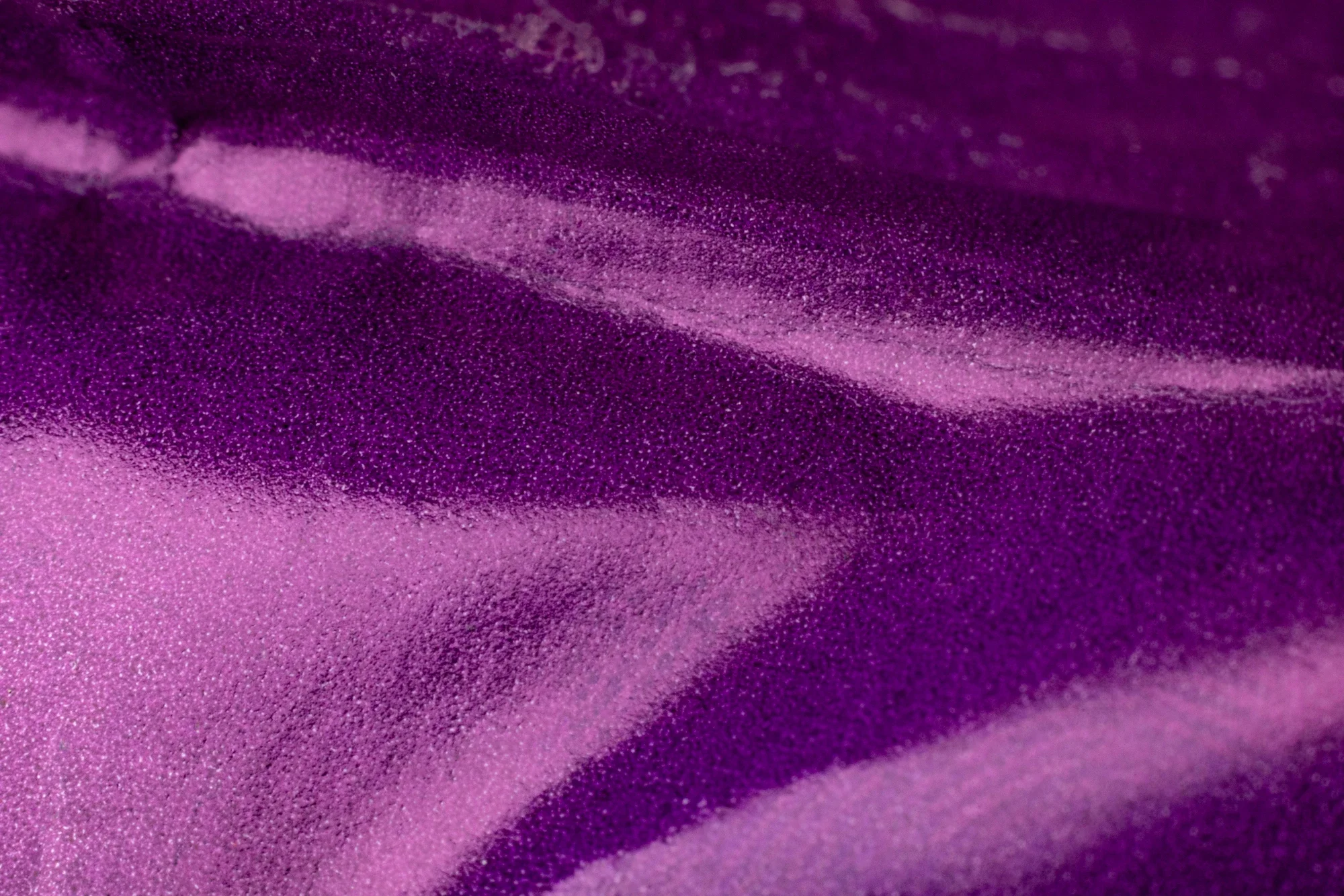 Zoom sur une surface violet foncé avec un motif de peinture ou de tissu imprimé, montrant des nuances de violet avec des reflets et des textures brillantes.