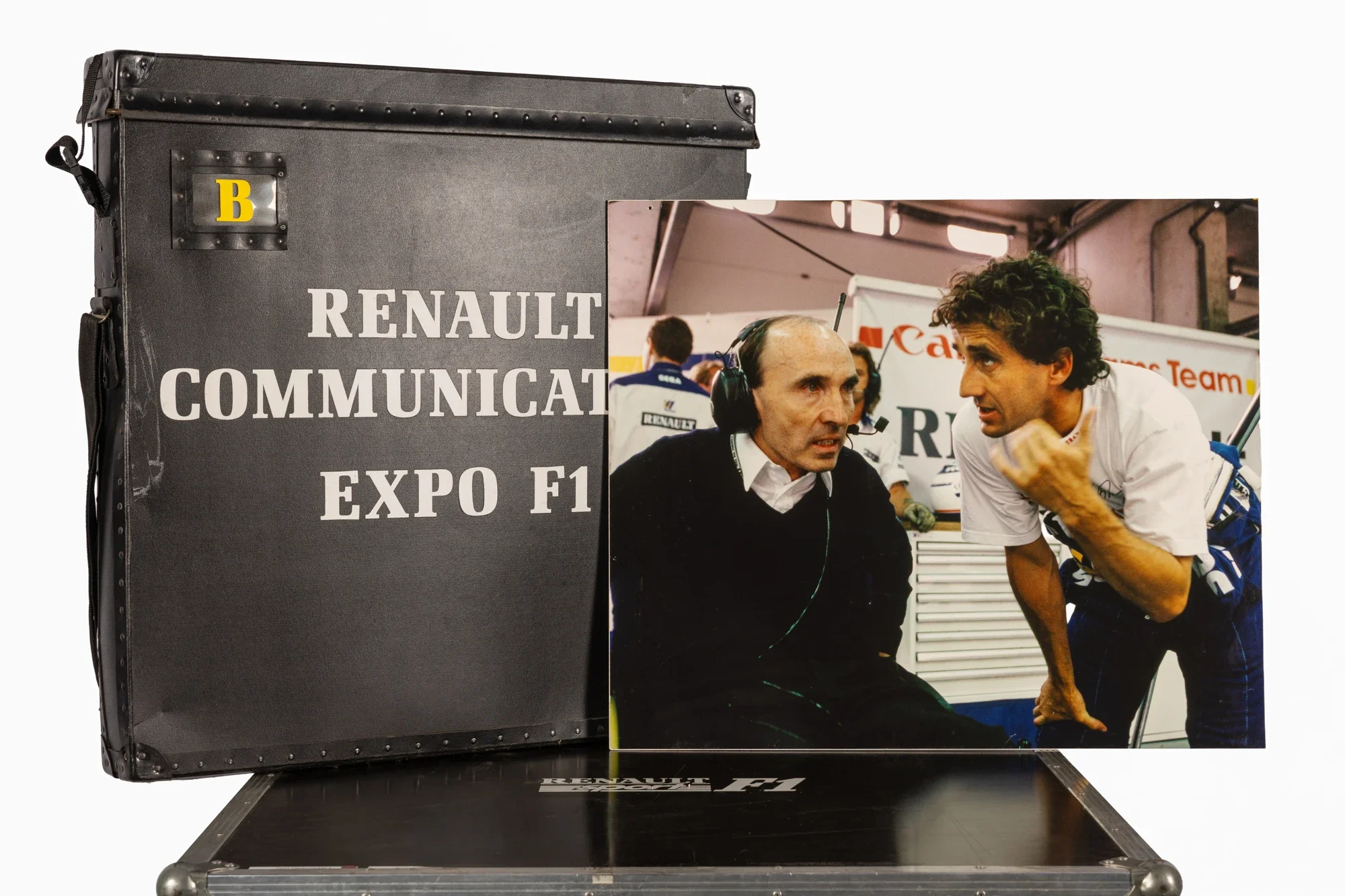 Une affiche de l'exposition Renault Communication Expo F1, affichant deux pilotes de Formule 1 en discussion dans un garage de course.