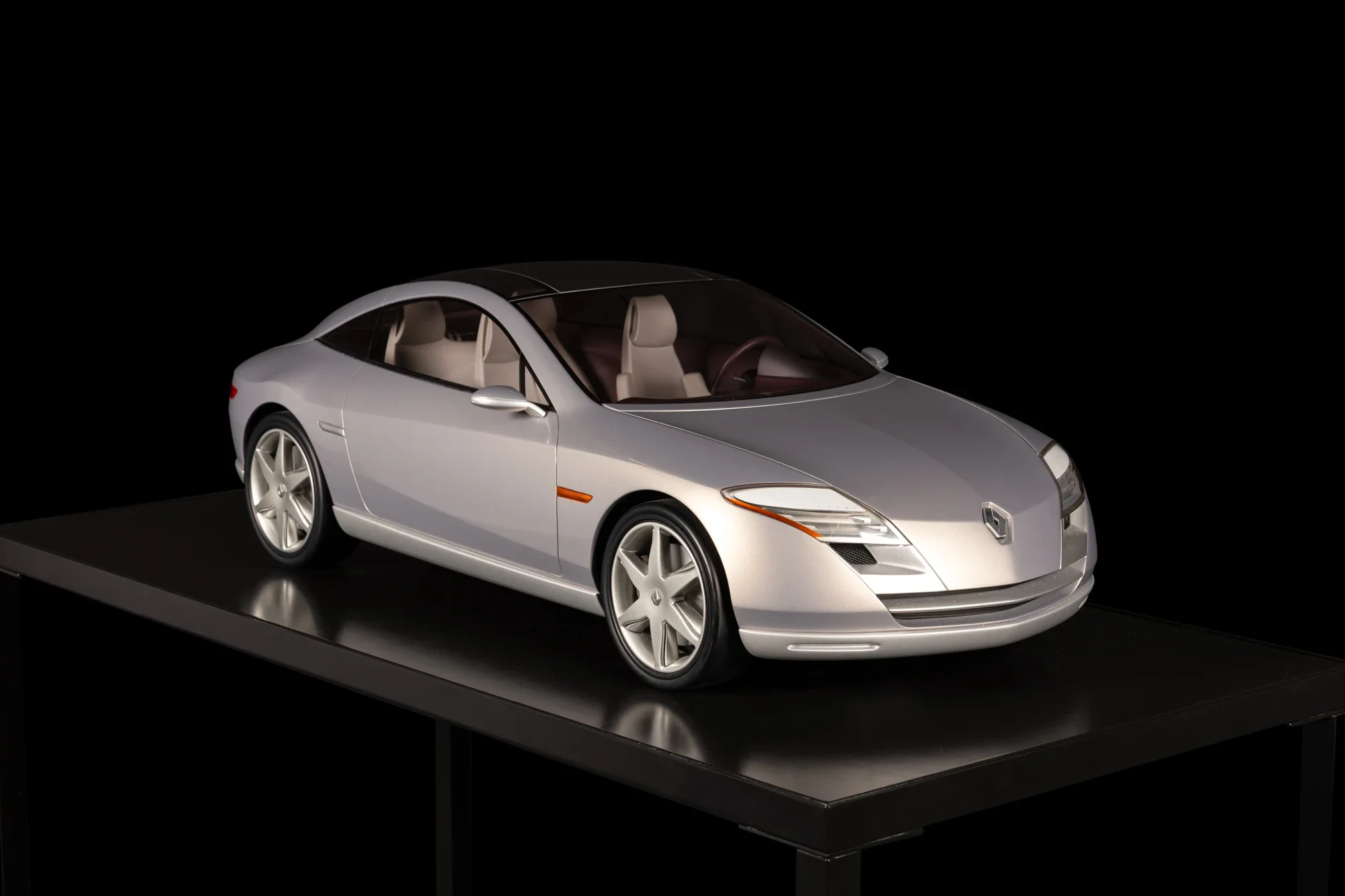 Modèle réduit de voiture Tesla Roadster sur un socle noir, vue de trois quarts avant, intérieur beige visible à travers le pare-brise et les fenêtres, fond noir