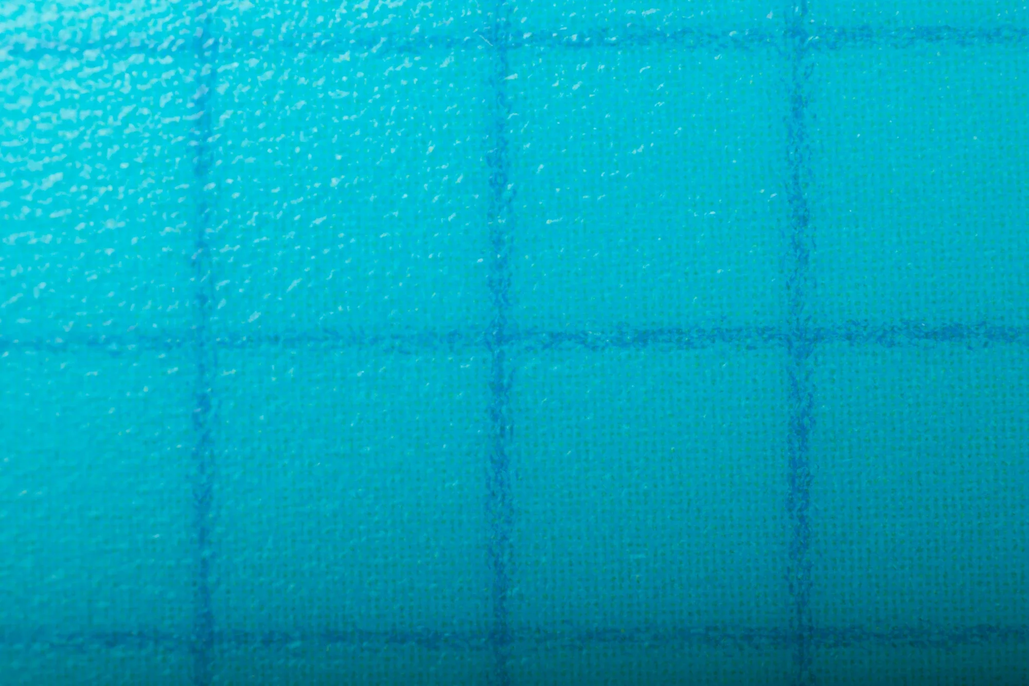 Close-up d'une surface en tissu turquoise avec une couture verticale visible.