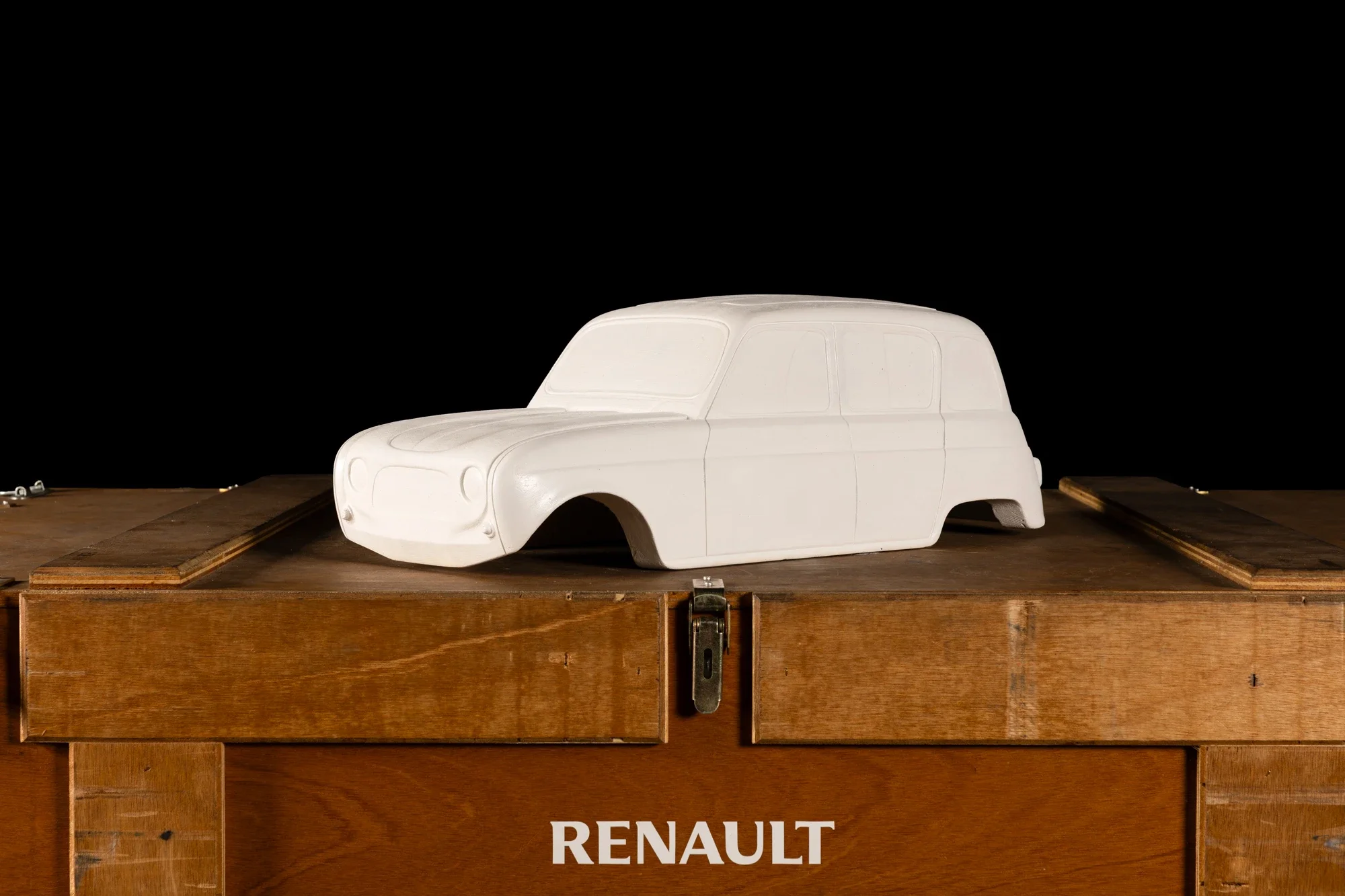 Modèle réduit blanc de voiture Renault, posé sur une étagère en bois, avec un fond noir.