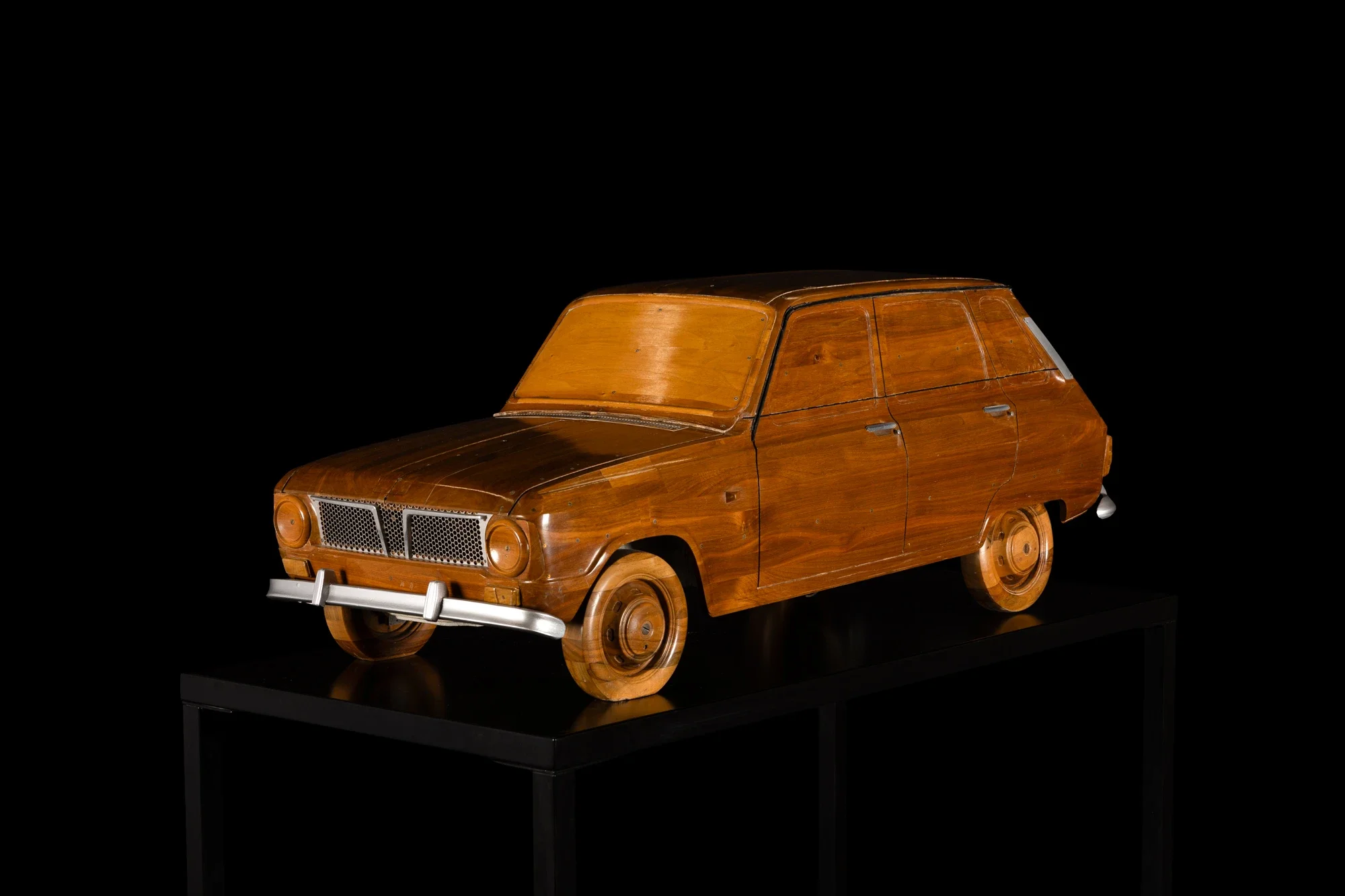 Voiture en bois sculpté exposée dans un musée, fond noir.