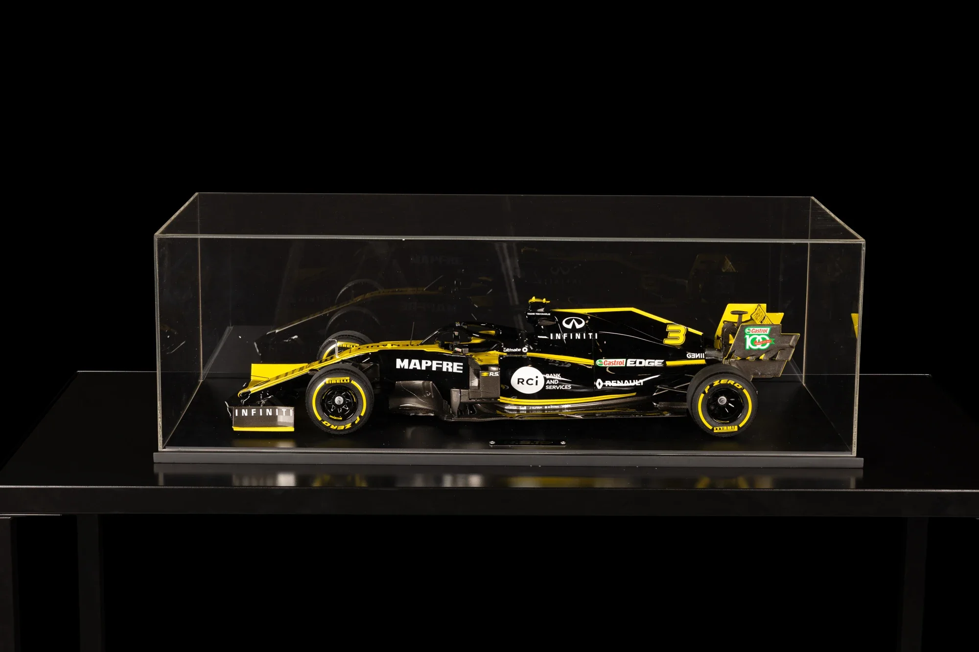 Une maquette d'une voiture de course rallye en miniature, noire avec des logos jaunes et blancs, dans une vitrine transparente sur un support noir.