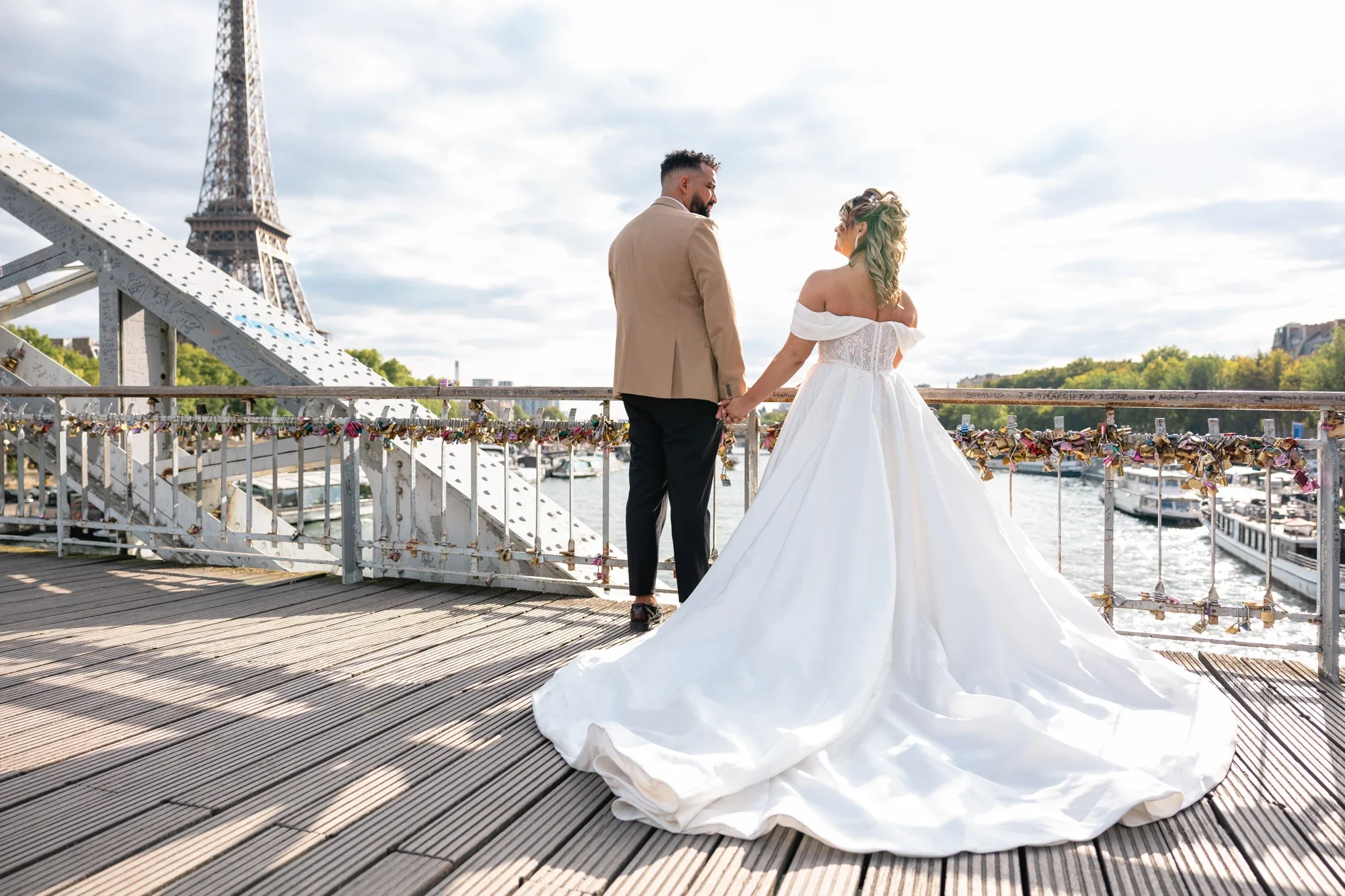 Un couple en vêtements de mariage sur un pont à Paris, avec la Tour Eiffel en arrière-plan, échangeant un regard.