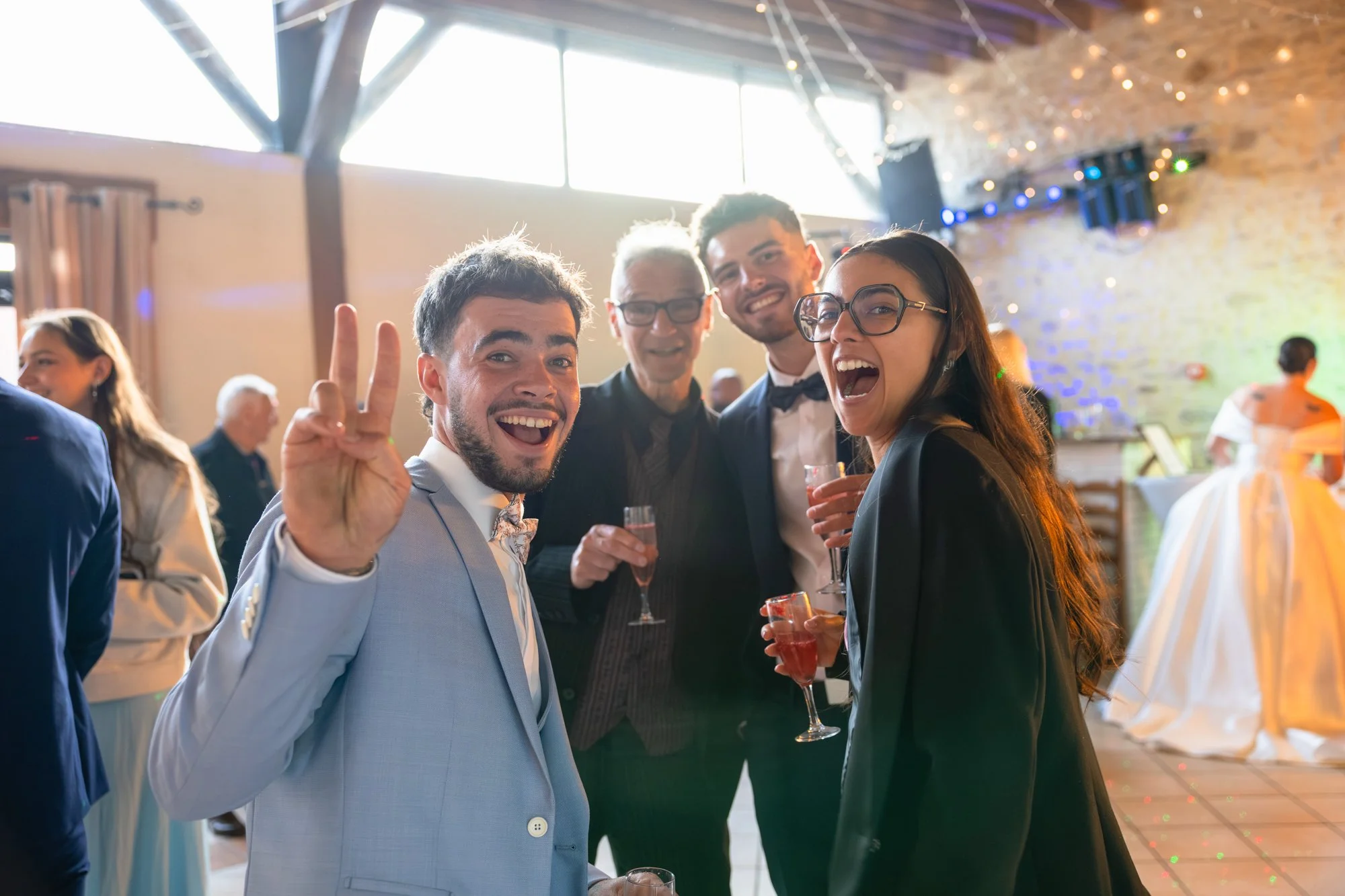 Groupe de cinq personnes souriantes lors d'une fête dans une salle décorée avec des lumières colorées, tenant des verres à cocktail.