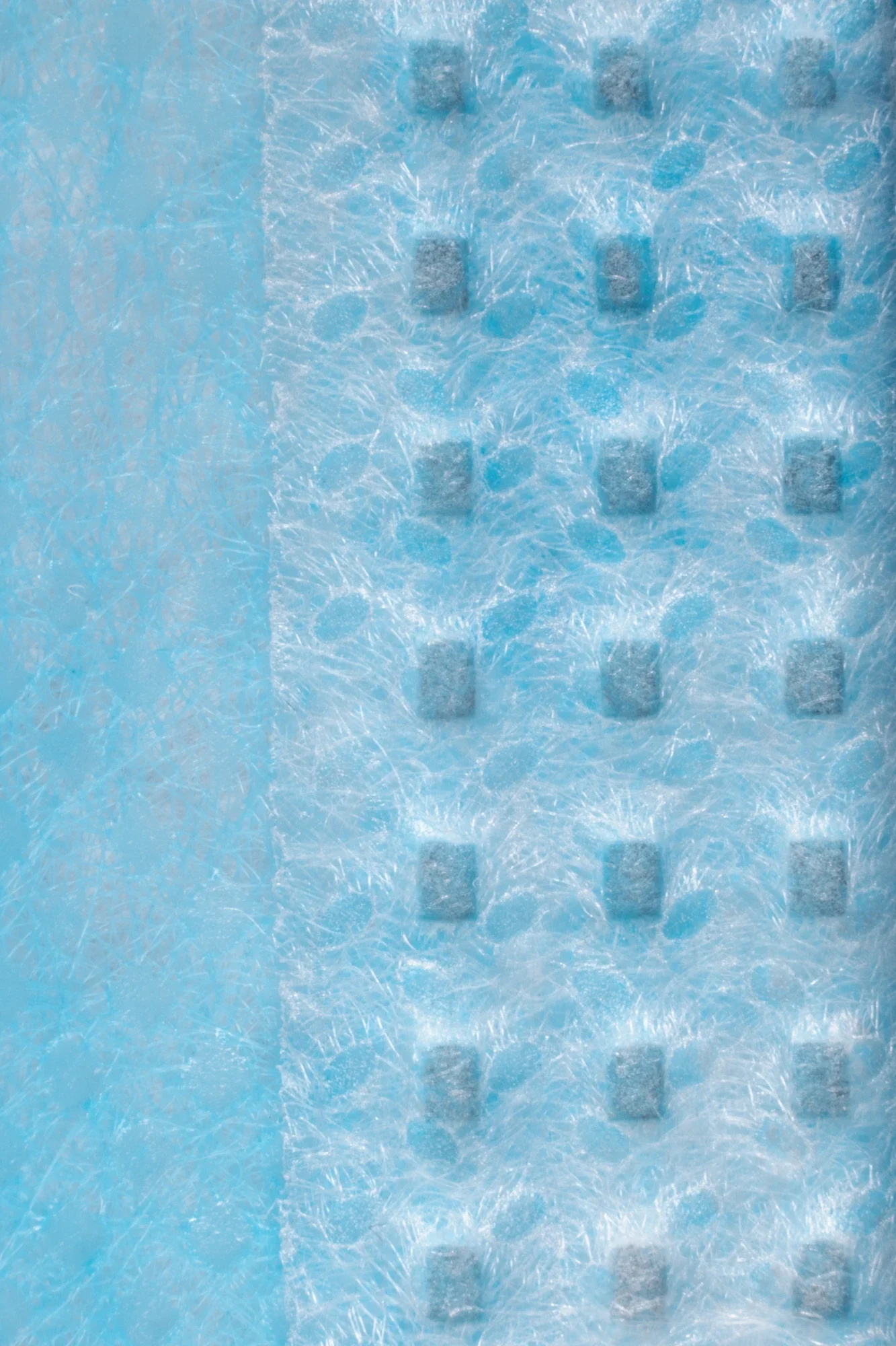Une surface bleue contenant des cristaux de glace et des capsules en forme de petits cubes gris.