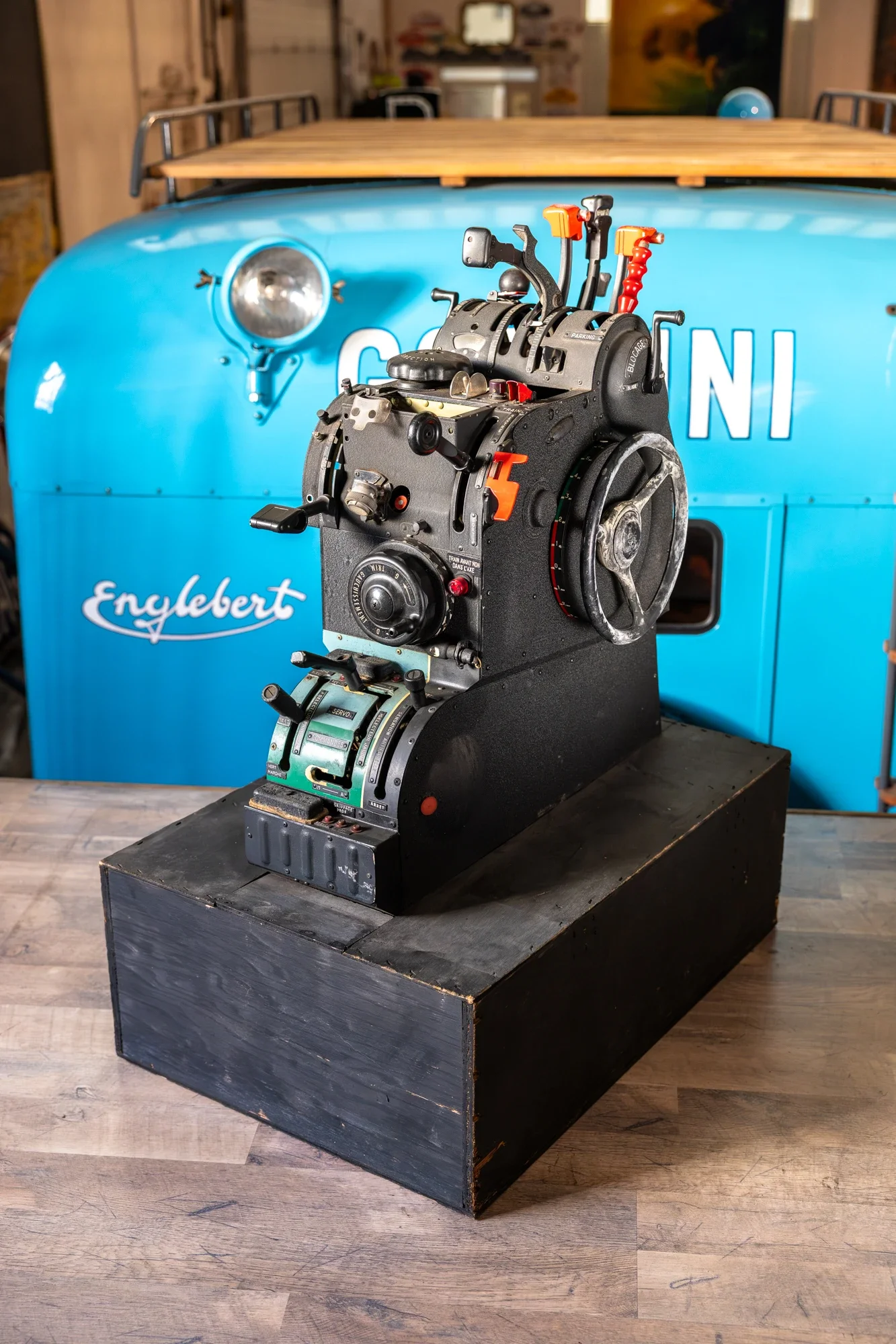 Un dispositif de pilotage de course ou un simulateur de vol en métal noir avec plusieurs leviers et boutons, placé sur une plateforme en bois foncé.