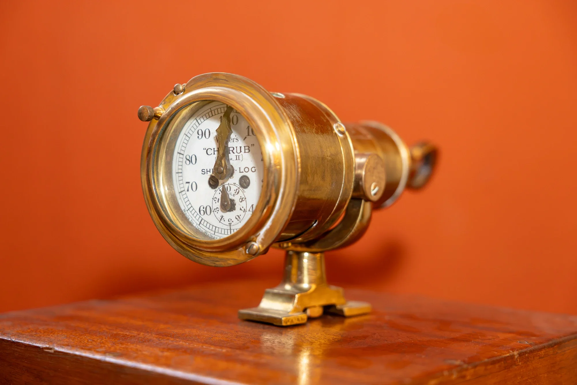Une horloge de style vintage en or, placée sur une surface en bois, avec un fond orange.