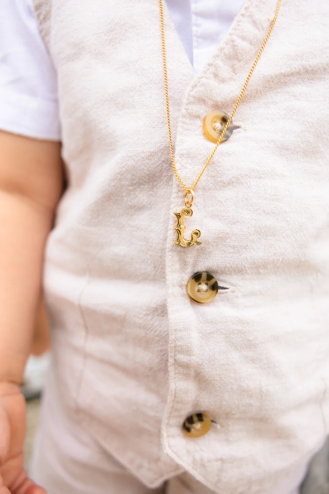 Un gros plan d'une personne portant une chemise blanche avec des boutons en tortoise. La personne porte un collier en chaîne dorée avec un pendentif en forme d'ancre gravé.