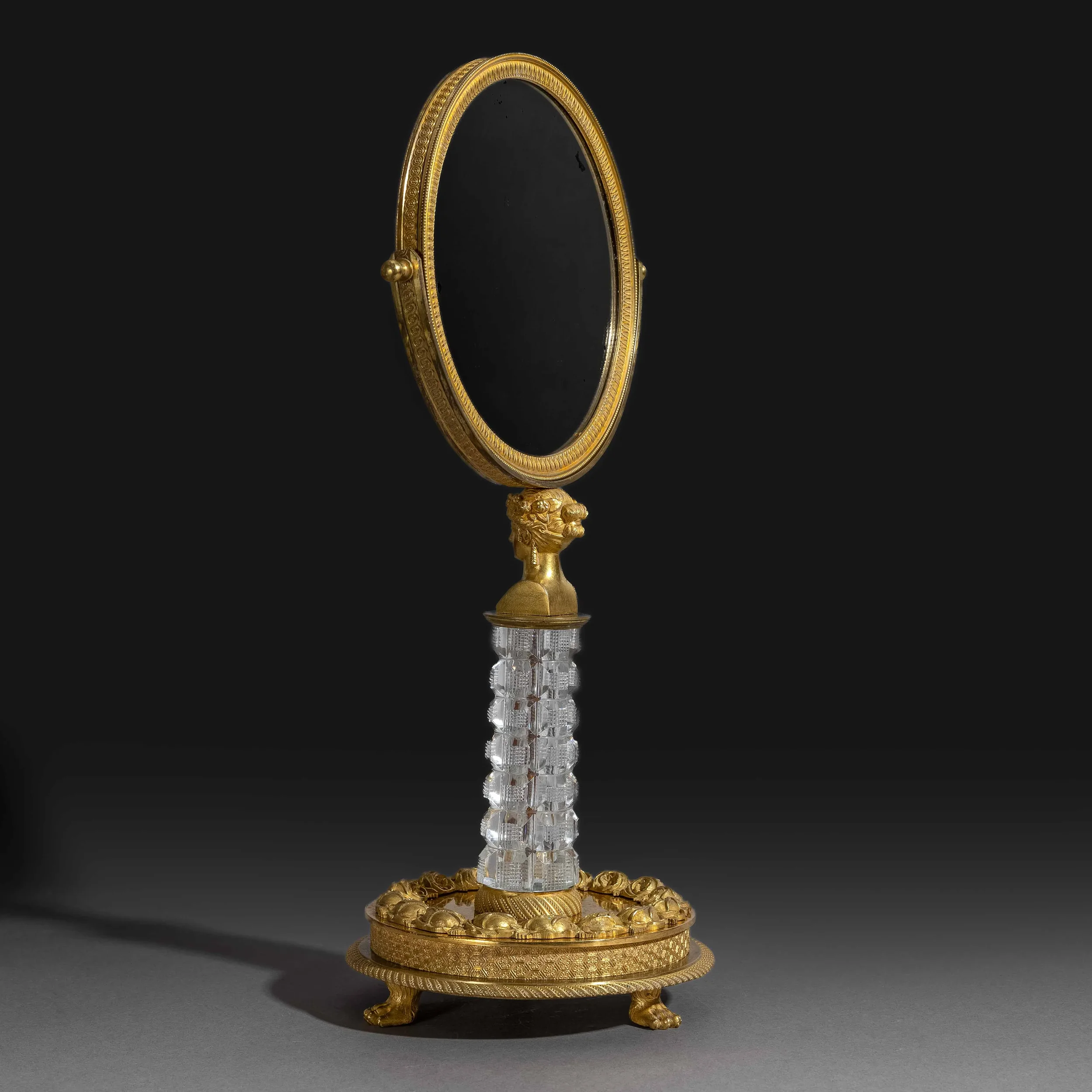 Miroir ovale encadré d'or avec décoration intricate, posé sur un support en or orné de motifs et de petits rosettes, reflet mystique sur fond noir