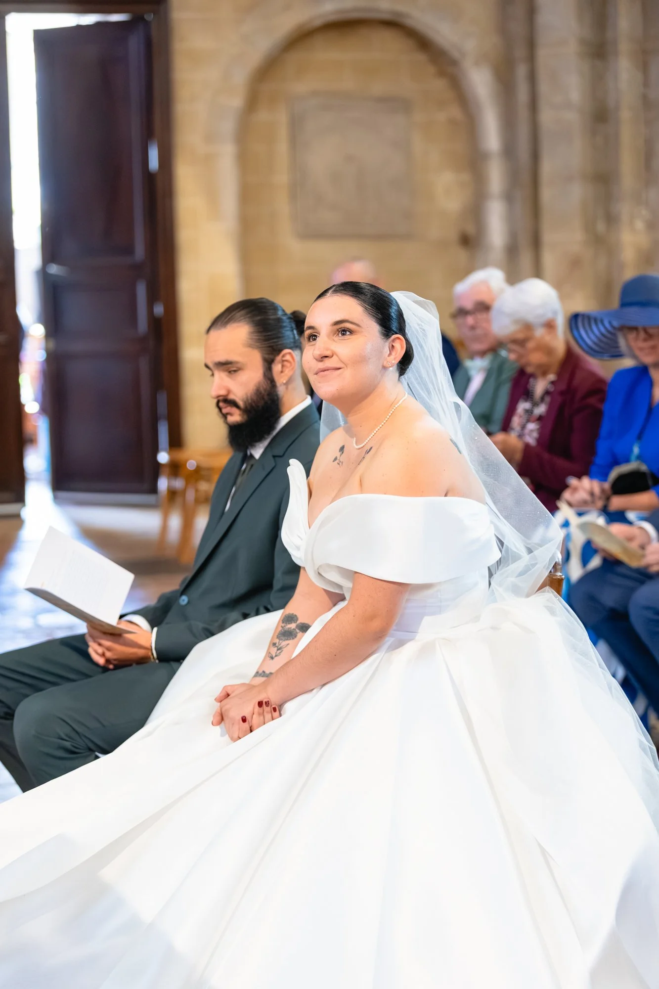 Un couple de mariage assis lors d'une cérémonie dans une église, entouré de leurs proches.