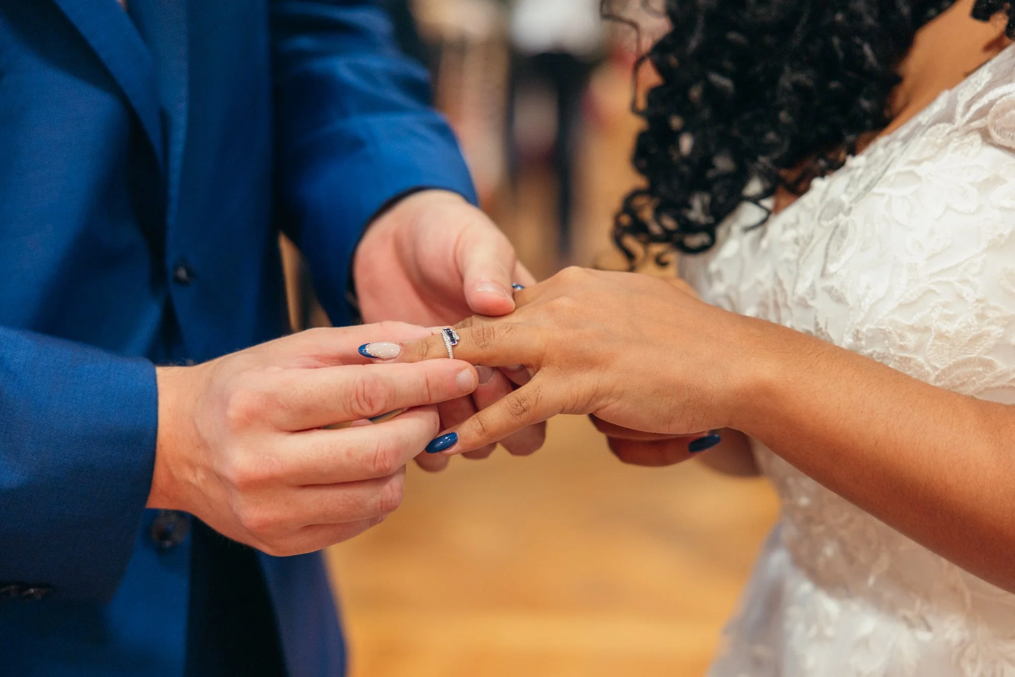 Une personne en costume bleu échange des anneaux avec une autre personne en robe blanche lors d'une cérémonie de mariage, échangeant des alliances.