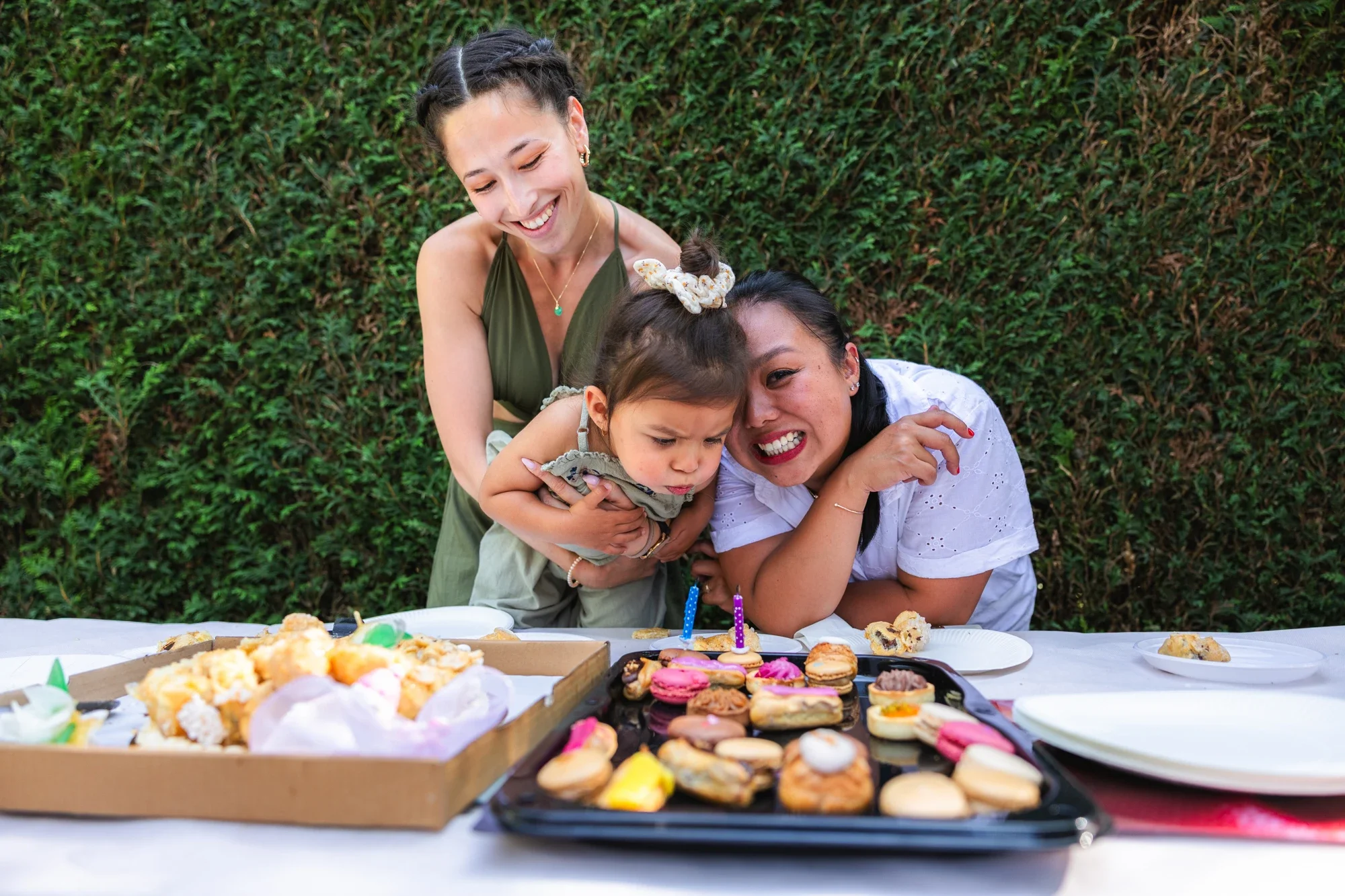 Trois femmes et un enfant ont une fête d'anniversaire dans un jardin avec une table de desserts, notamment des cupcakes et des biscuits.