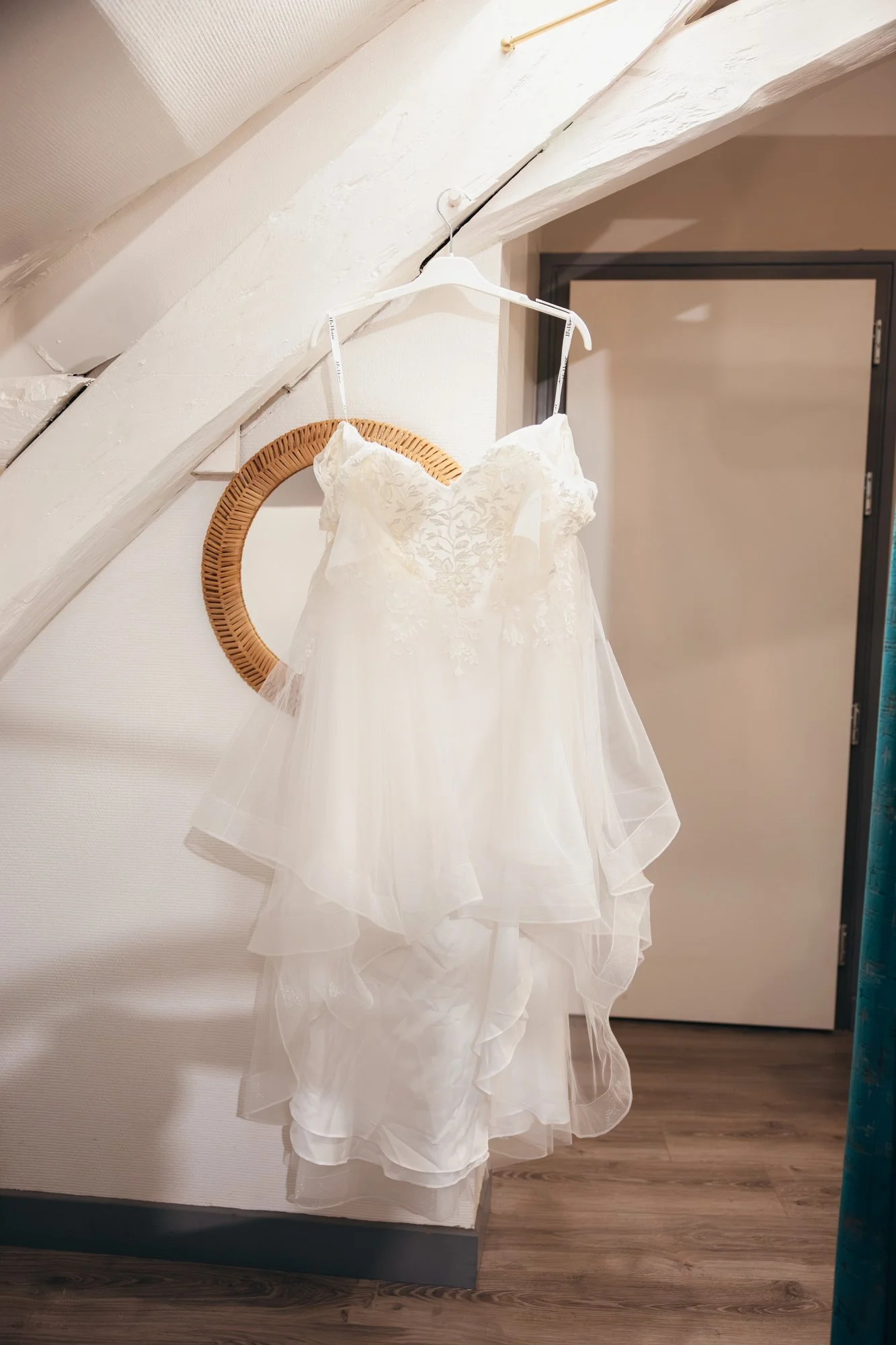 Une robe de mariage blanche suspendue à un cintre blanc, accrochée à une branche en bois. La robe est en tissu léger avec des détails en dentelle sur le haut et une jupe fluide en tulle.