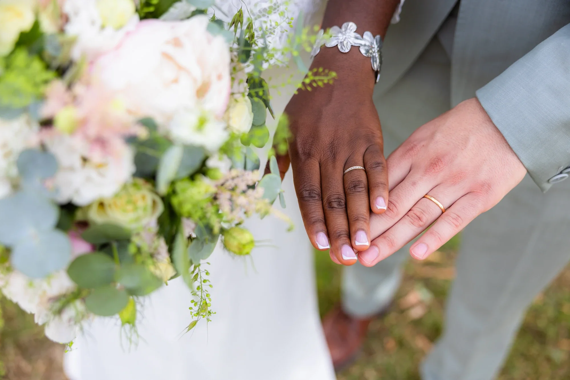 Deux mains, une masculine et une féminine, jointes lors d'une union nuptiale, avec des alliances, entourées de fleurs de mariage.