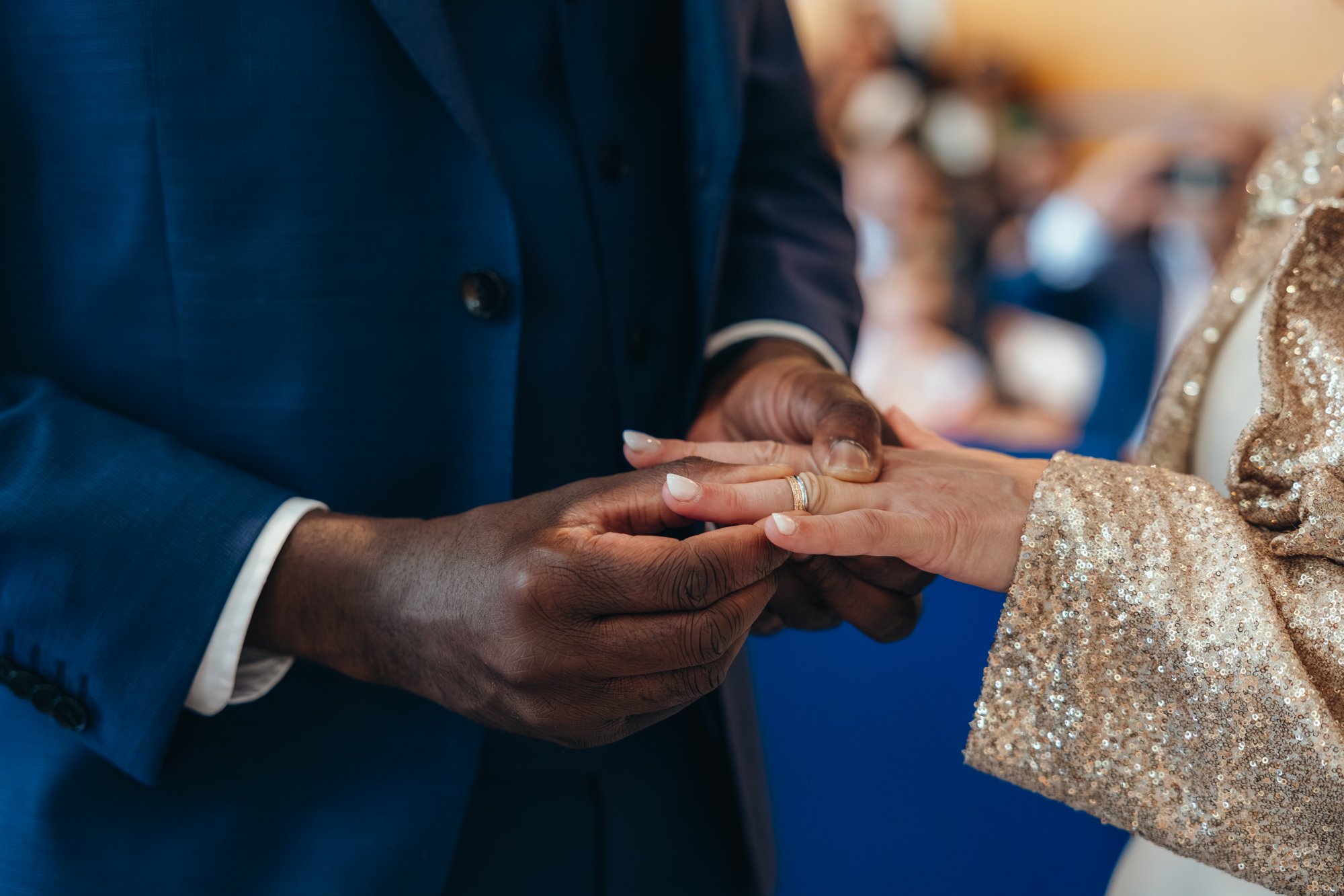 Une personne en costume sombre tenant la main d'une autre personne habillée en robe de soirée or rose avec des paillettes.