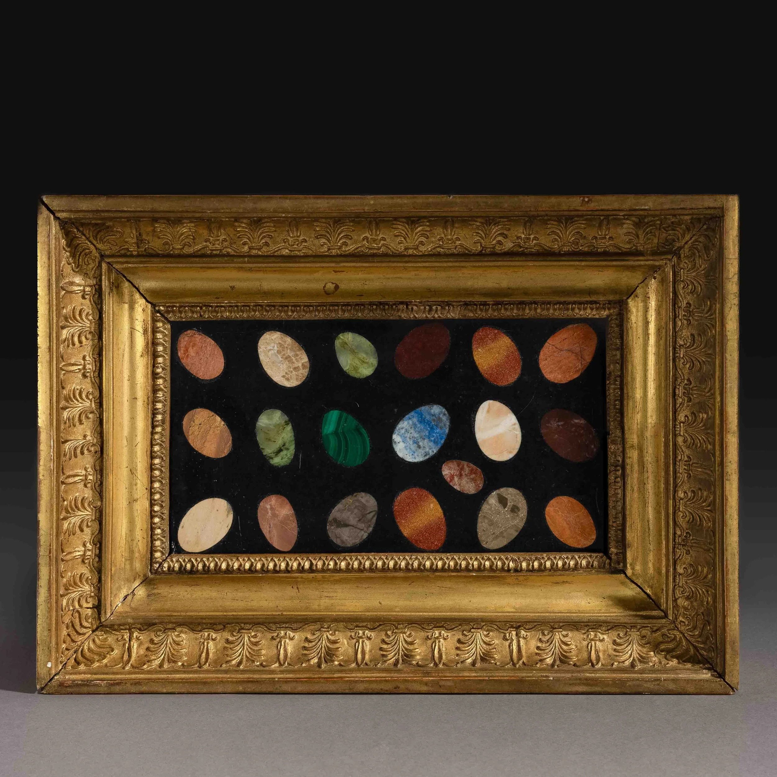 Un cadre doré orné de motifs décoratifs entourant une œuvre d'art contenant une collection de pierres précieuses colorées.