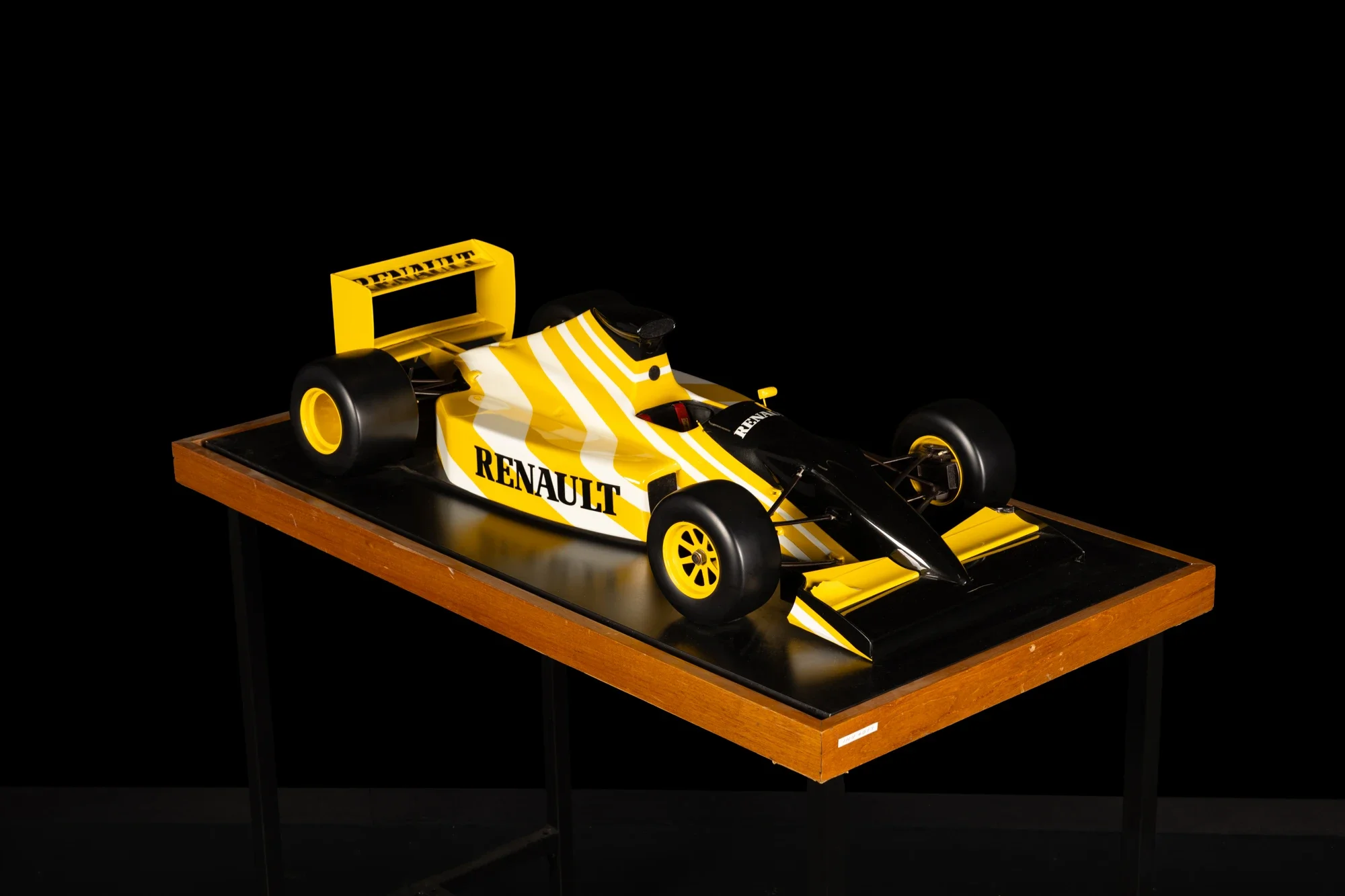 Modèle réduit de voiture de course Renault yellow and black sur une table en bois, fond noir.