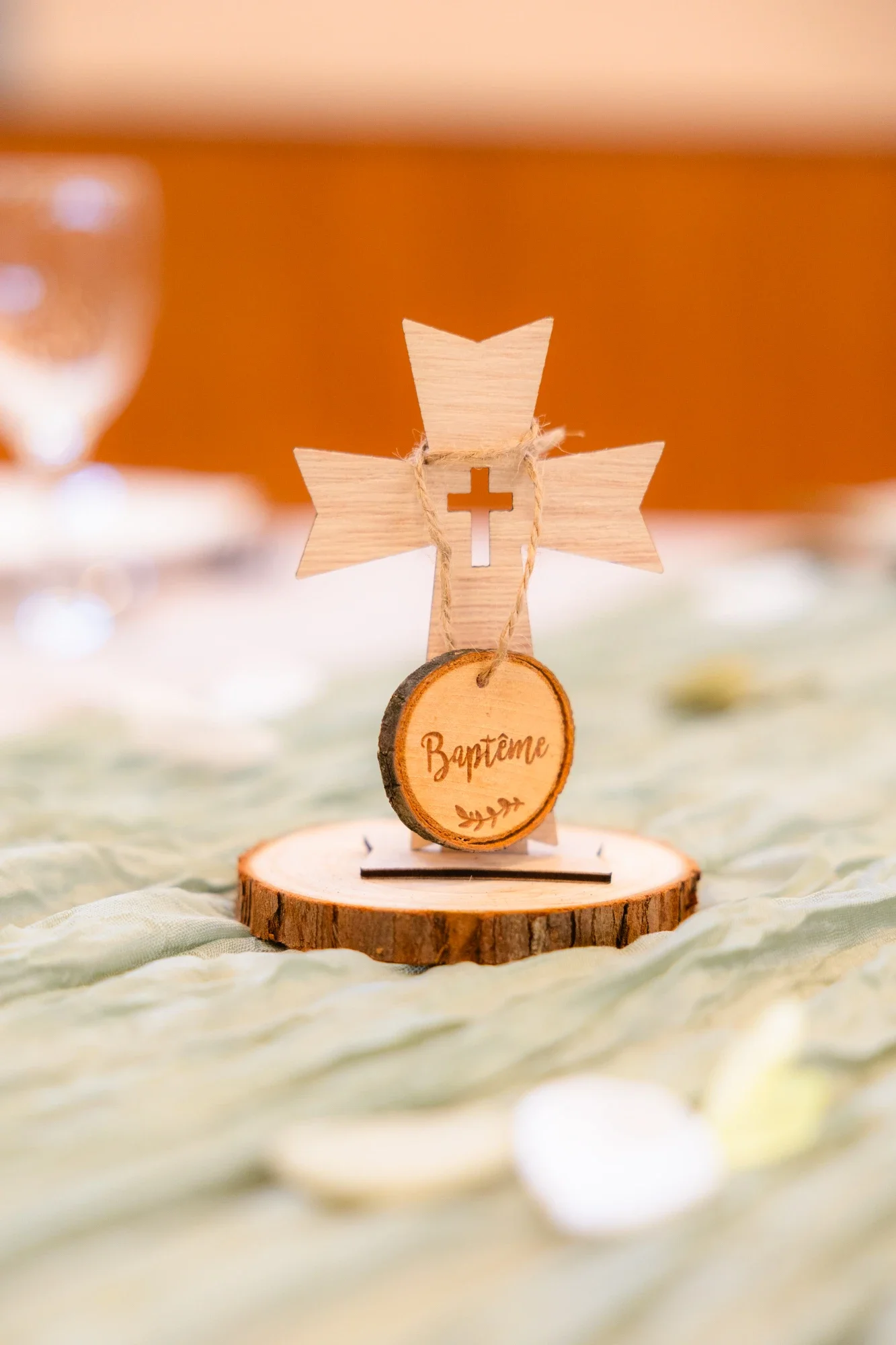 Décoration de baptême en bois avec une croix, un cercle avec "Baptême" gravé, et une étoile en bois, placée sur une tranche d'arbre.