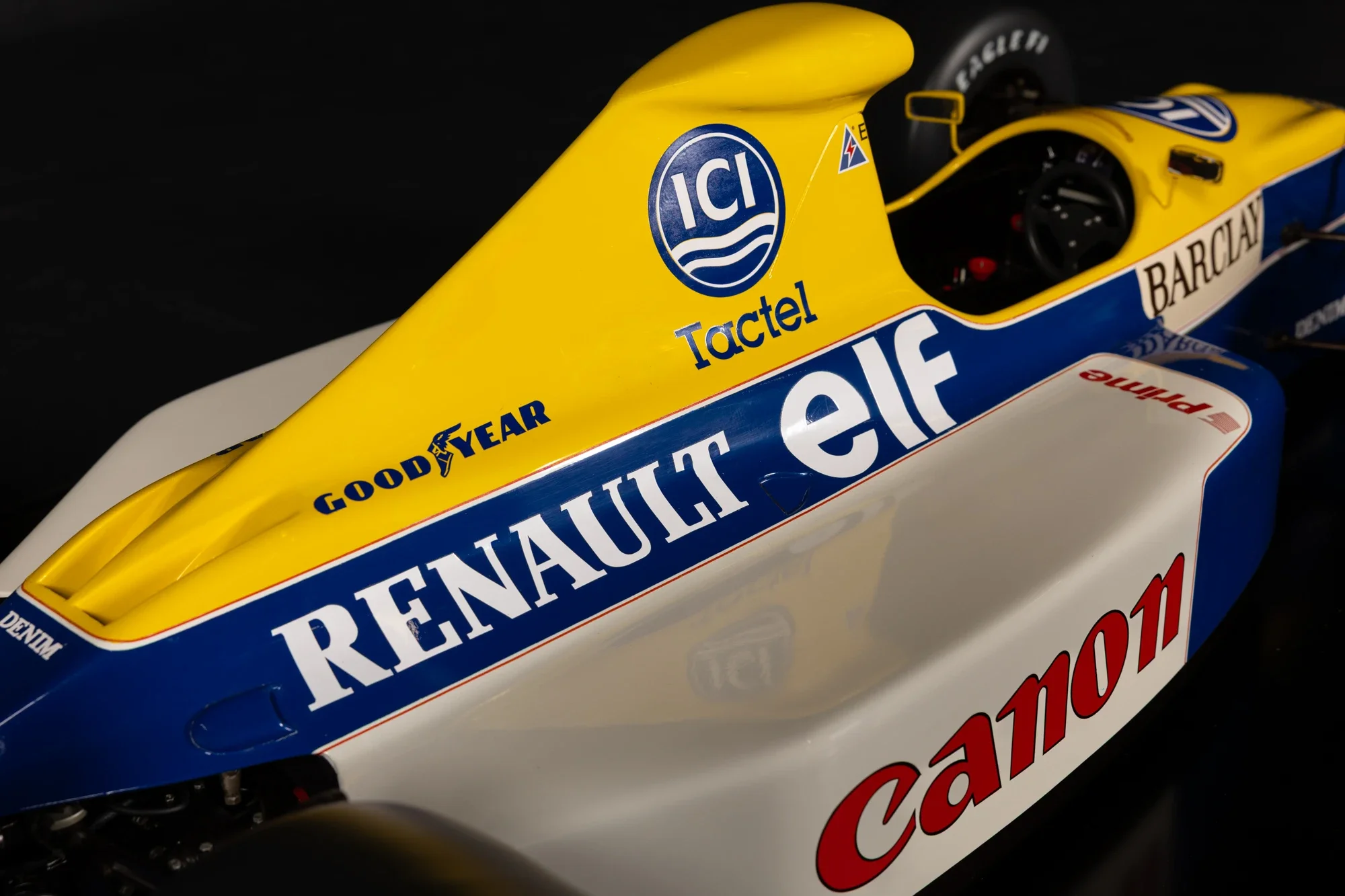 Détails d'une voiture de course avec des logos et des sponsors, principalement en jaune, bleu et blanc.