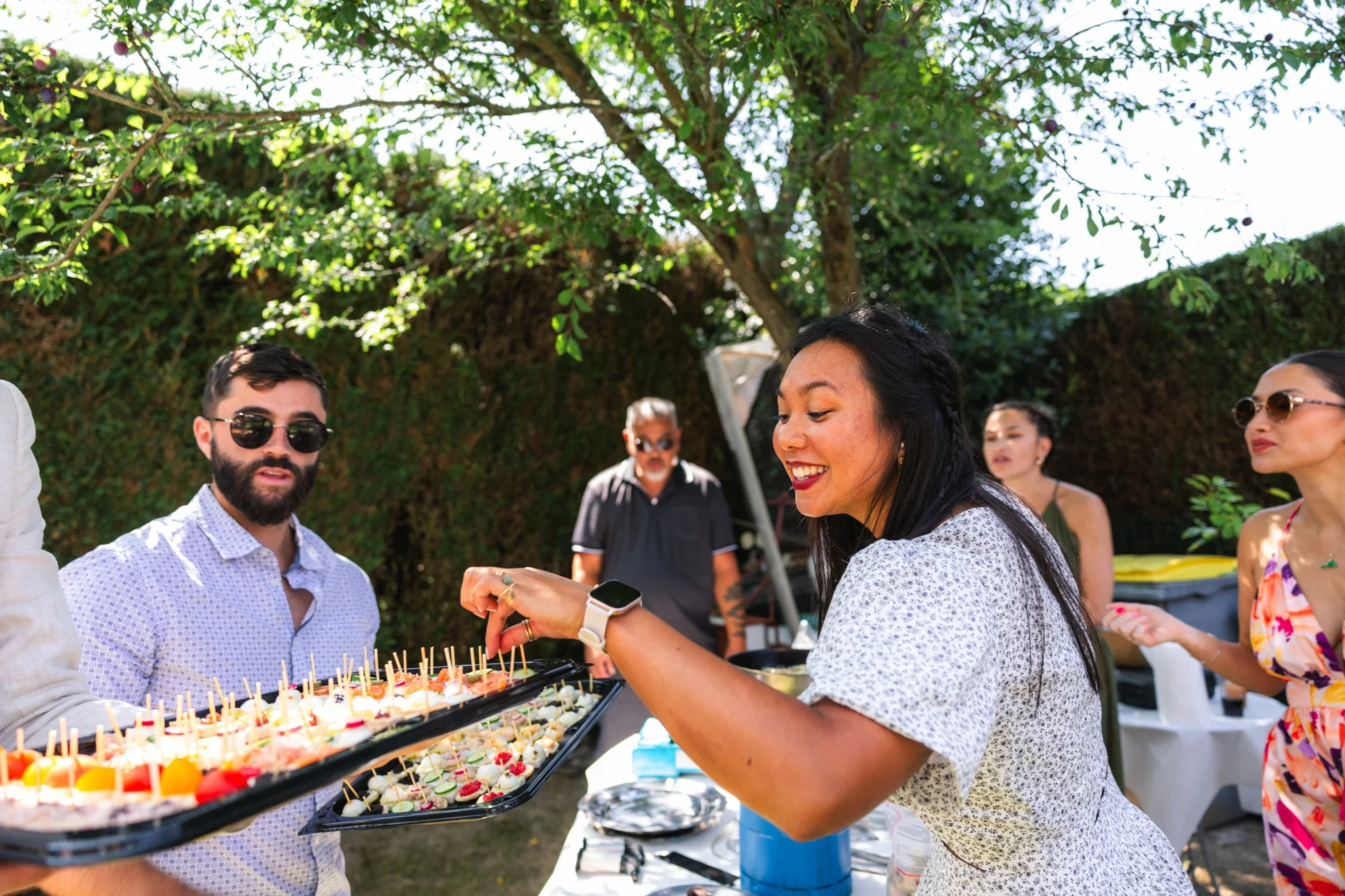 Groupe de personnes lors d'une fête en extérieur avec un buffet de mini-bouchées décorées, ambiance conviviale.